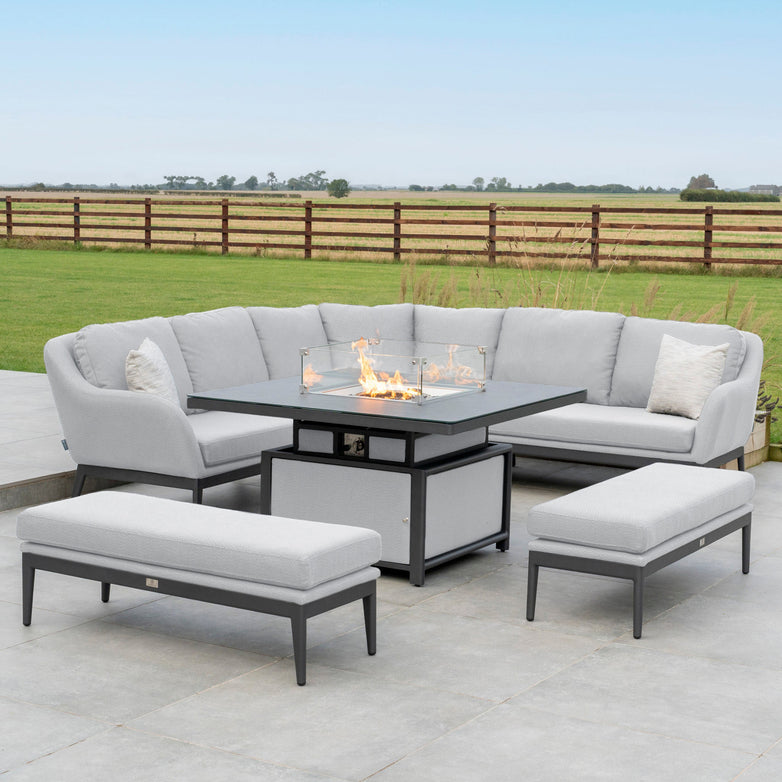 Outdoor patio with a Luna Deluxe Outdoor Fabric Square Corner Dining Set featuring a Rising Firepit Table in Oyster Grey, set against the backdrop of a large grassy field.