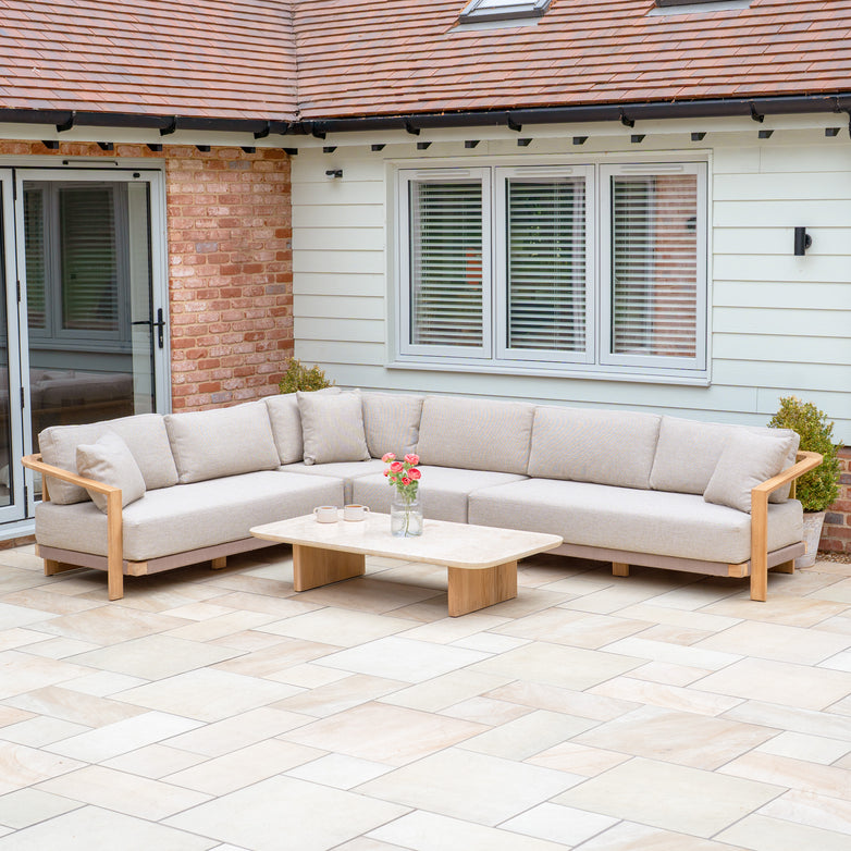 The Tivoli Large Corner Set with Marble Coffee Table in Fawn is arranged on a tiled patio outside a house with pale siding.