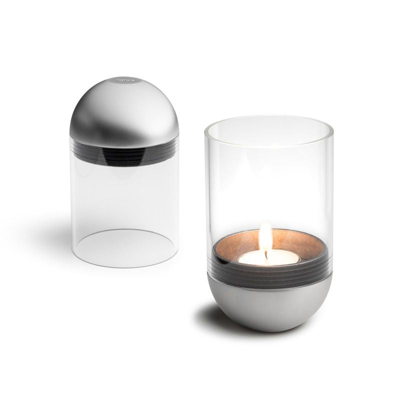 Two modern glass candle holders with metallic bases, one with a lid and one glowing softly, similar to the Höfats GRAVITY CANDLE Lantern.