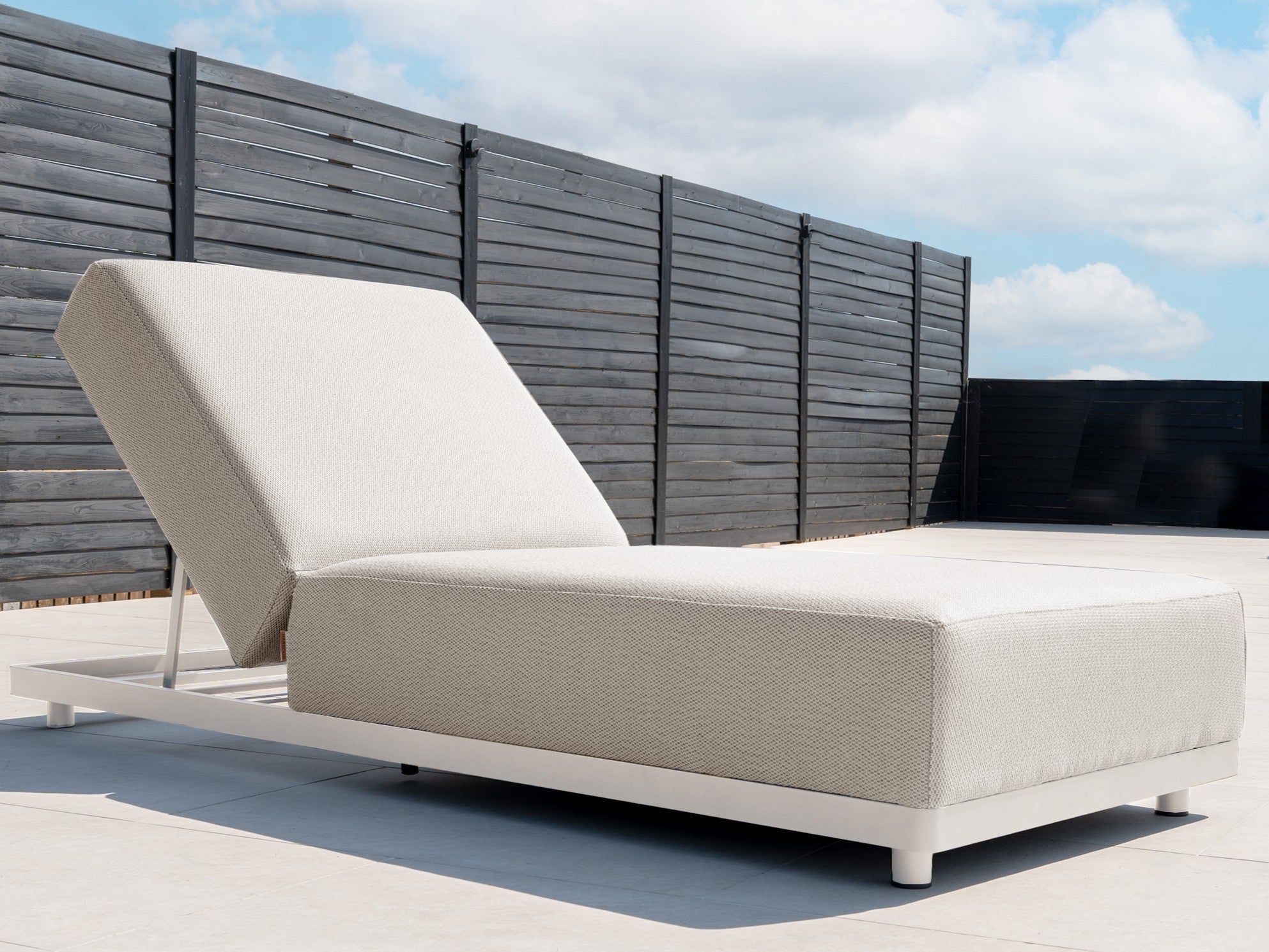 A deluxe Luna sunlounger poolside with a fence behind it.