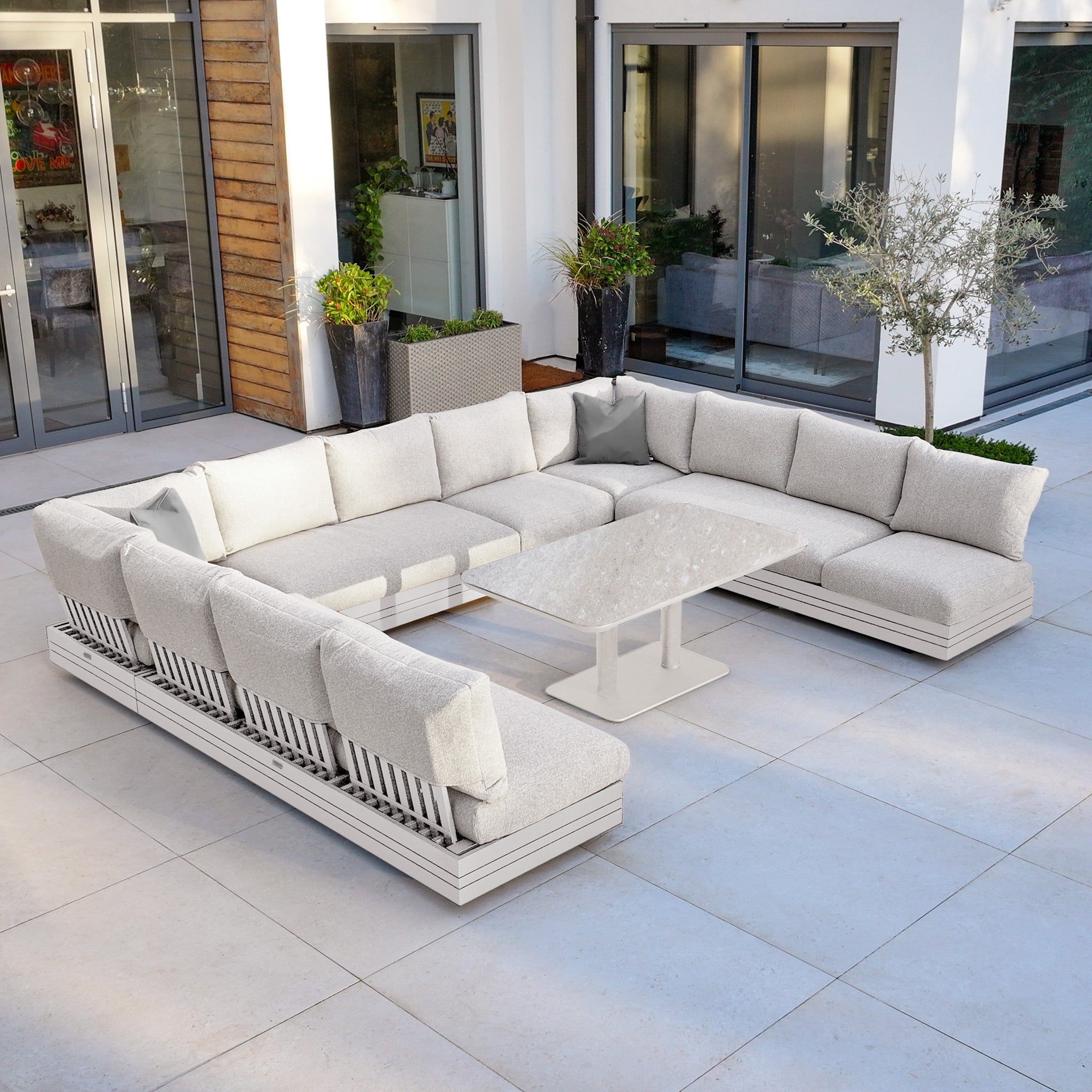 Modern outdoor patio with a large white sectional sofa and a rectangular table on a tiled floor.