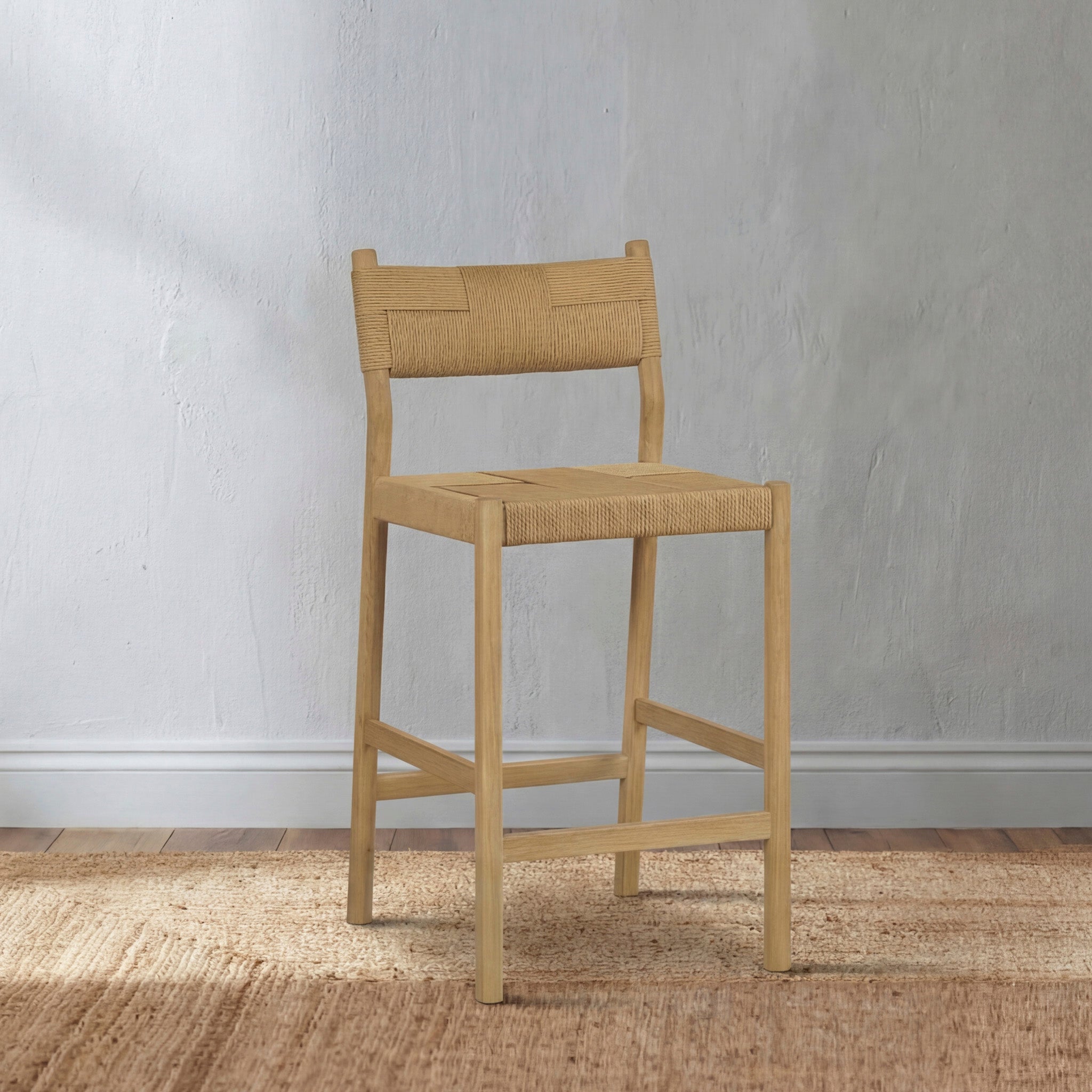 A wooden bar stool with a woven seat and backrest on a rug against a light gray textured wall.