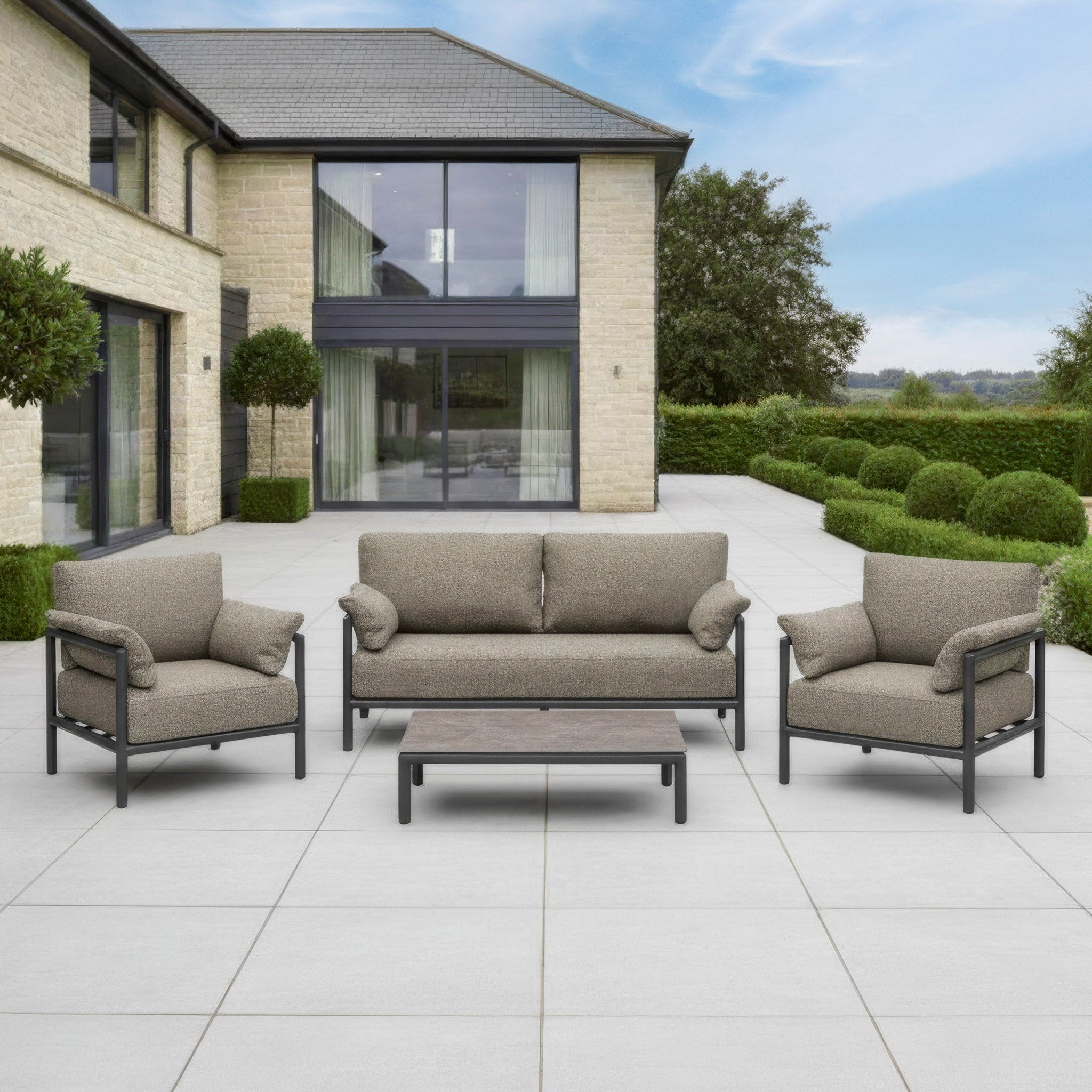 Modern outdoor patio set with sofa, two armchairs, and a coffee table on a large tiled terrace.