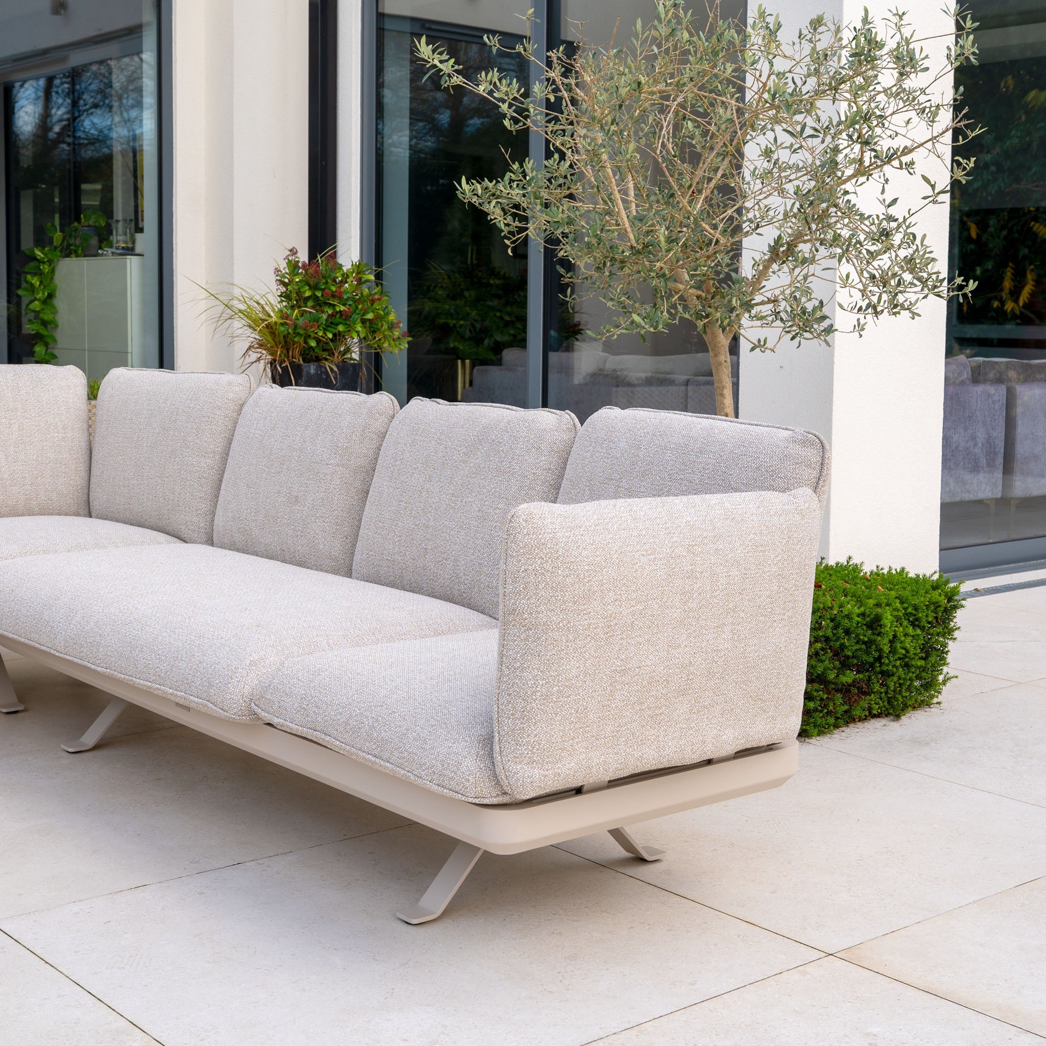 Outdoor patio with beige cushioned chairs, sofa, round table, and brick wall with large glass doors.