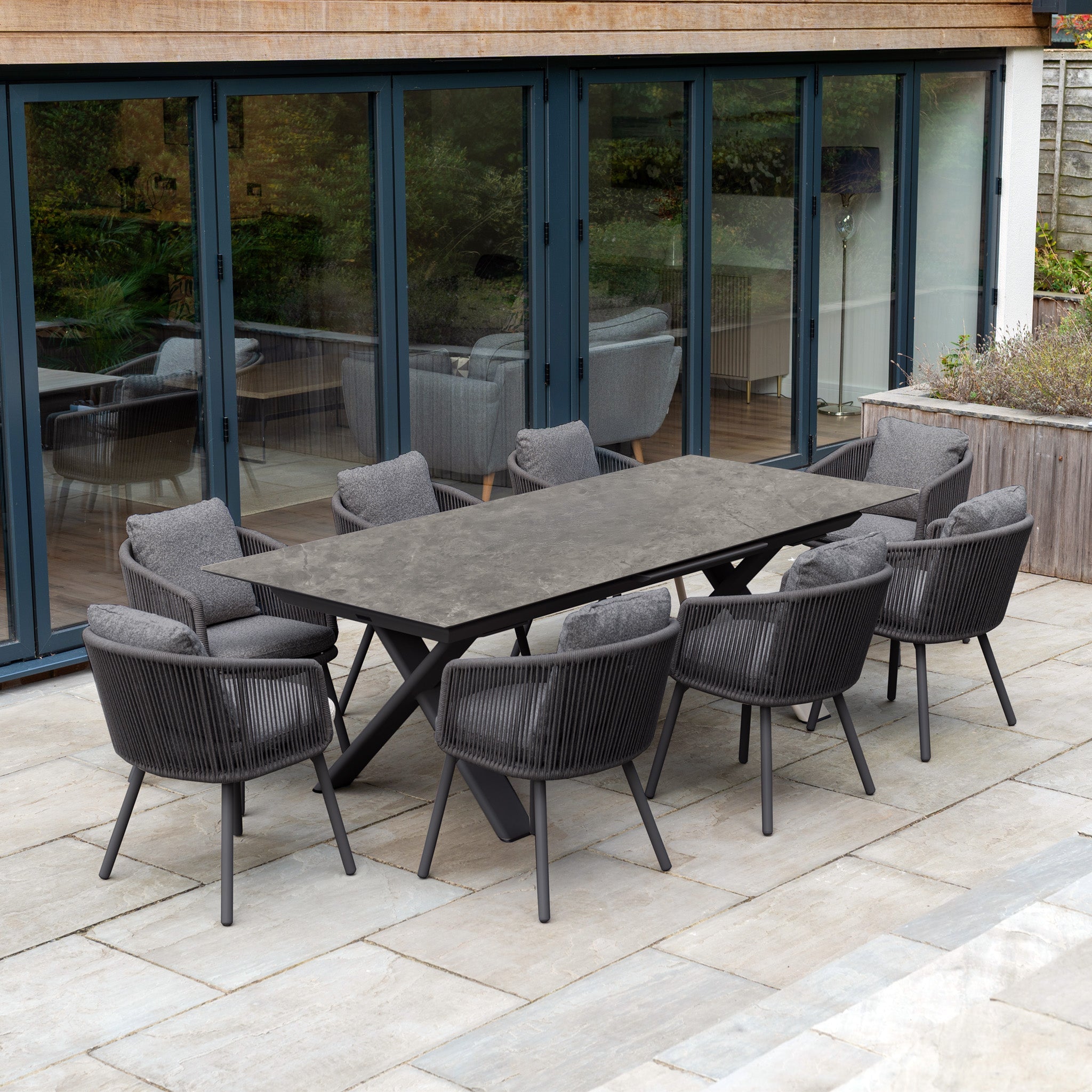Modern patio with beige outdoor sofa, two chairs, and coffee table set on stone tiles outside a house.