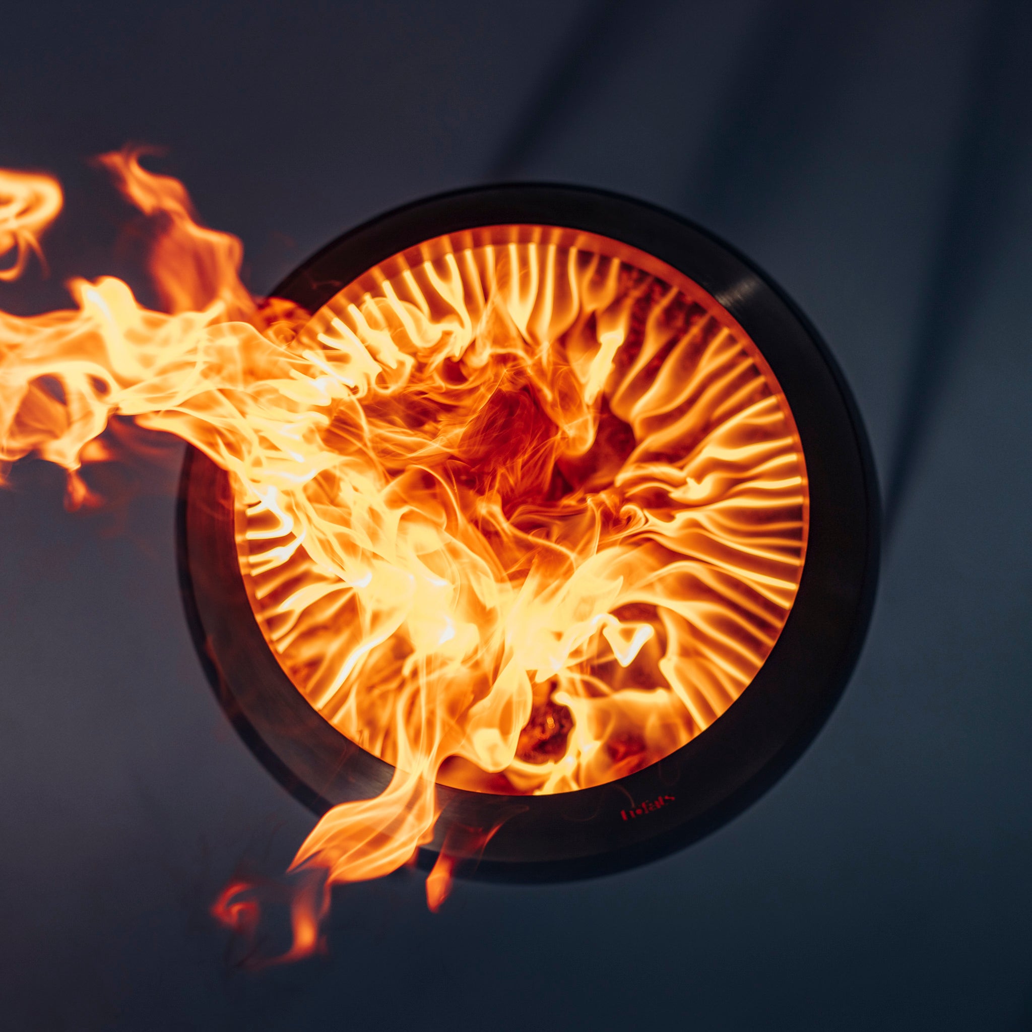 Top view of the Höfats MOON 45 Fire Bowl with Low Stand, showcasing swirling flames and featuring black fire art against a dark background.