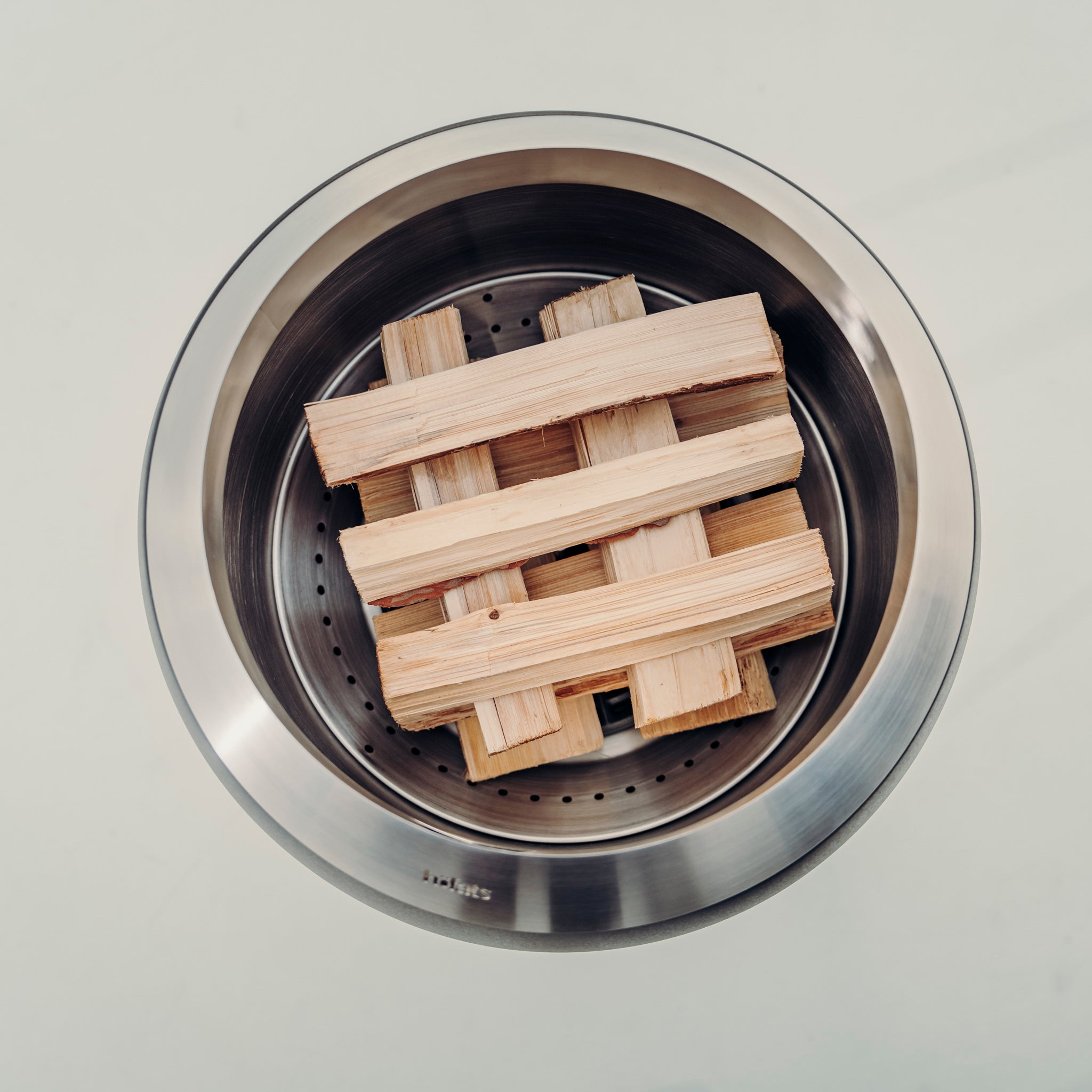 Höfats MOON 45 Fire Bowl with High Stand featuring a stack of wood pieces arranged in a crisscross pattern, viewed from above, showcasing a hint of wood gasification.