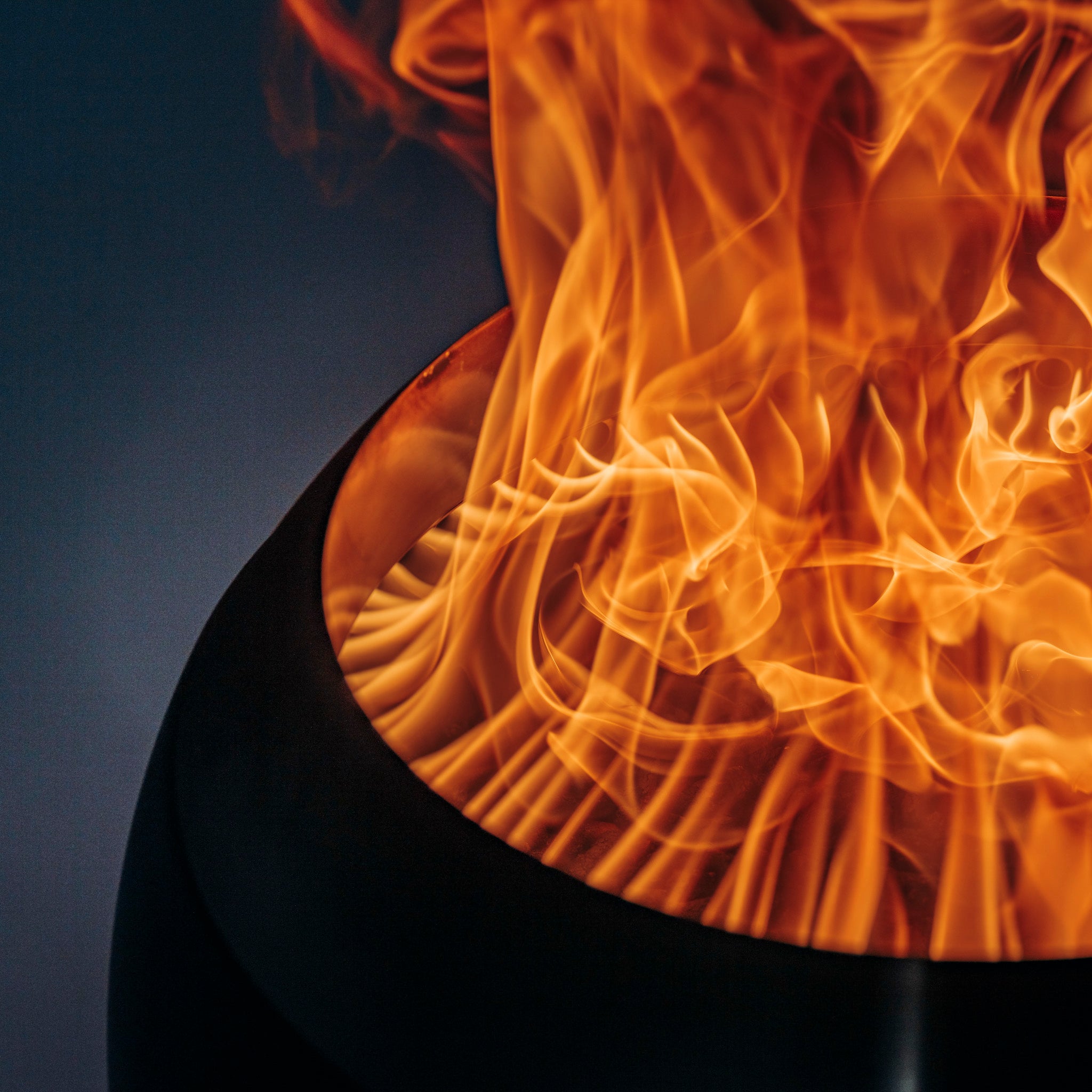 Close-up of a vibrant, swirling fire inside the Höfats MOON 45 Fire Bowl with High Stand against a dim background, showcasing revolutionary combustion technology.