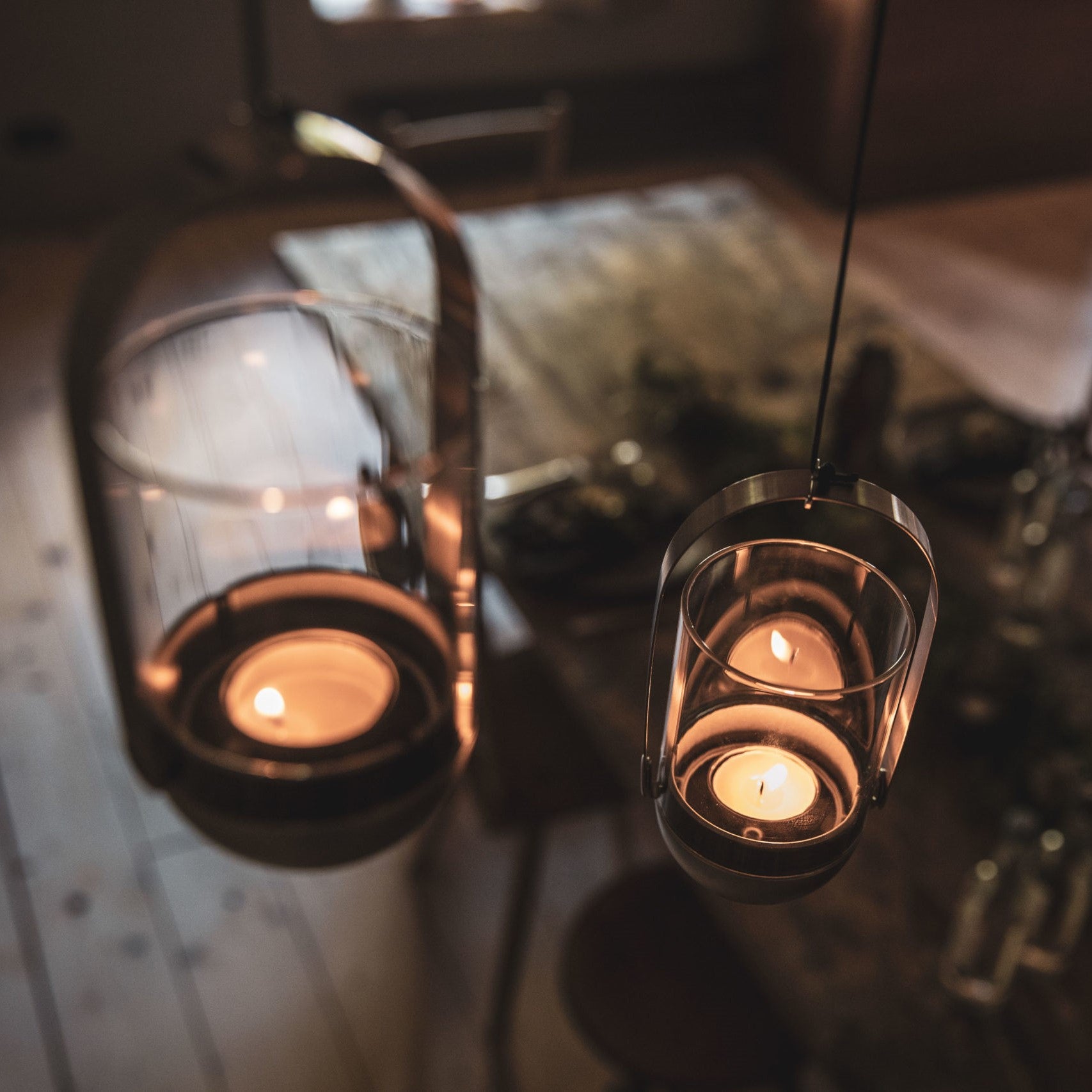 Hanging lanterns with lit candles illuminate a cozy, wooden dining table set for a meal, enhanced by the warmth of the Höfats GRAVITY CANDLE Hanger and the elegance of brushed solid stainless steel.