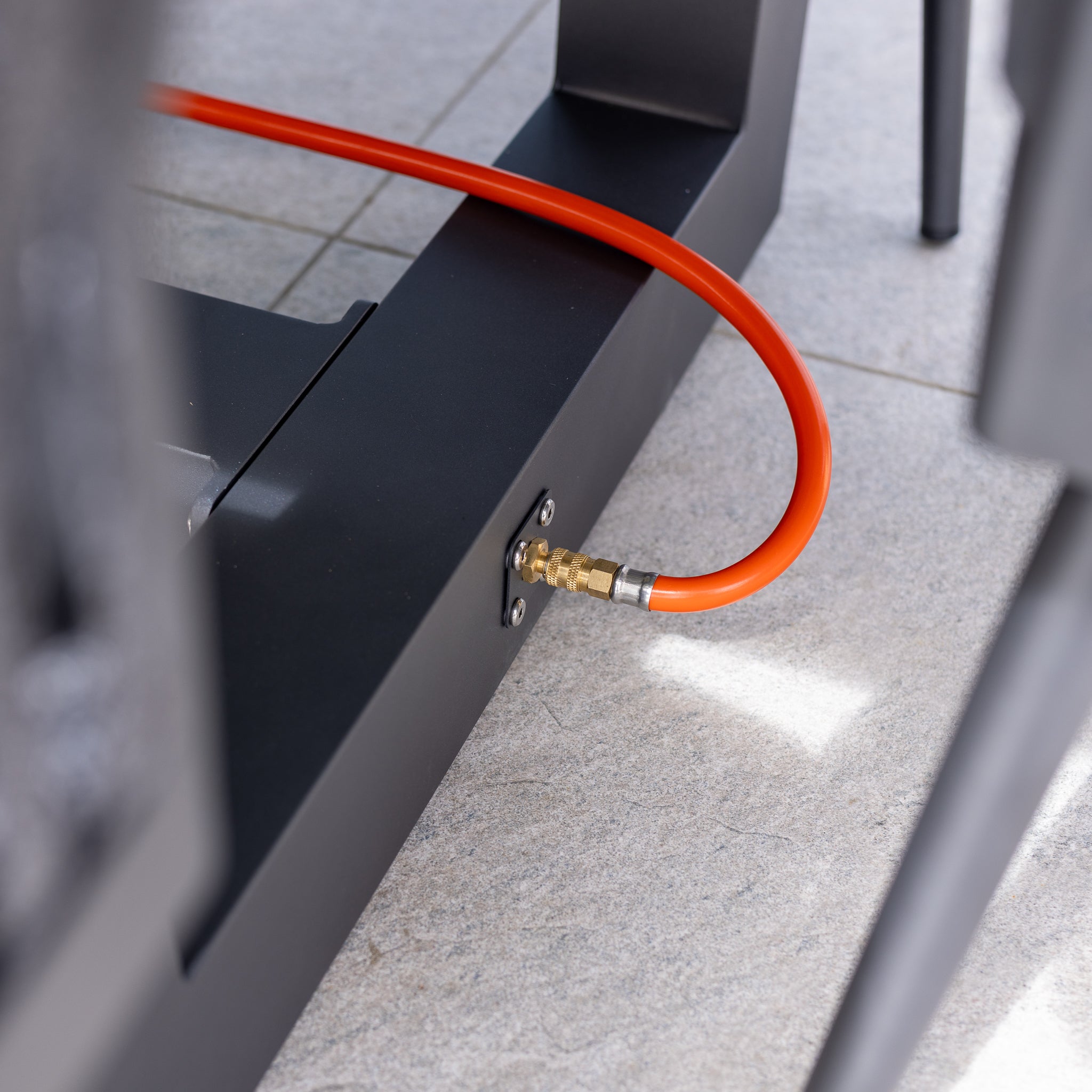 Close-up of an orange cable connected to a black metal structure on a tiled floor, situated near the all-weather material of the Luna 8 Seat Outdoor Fabric Rectangular Ceramic Firepit Dining Set in Grey.