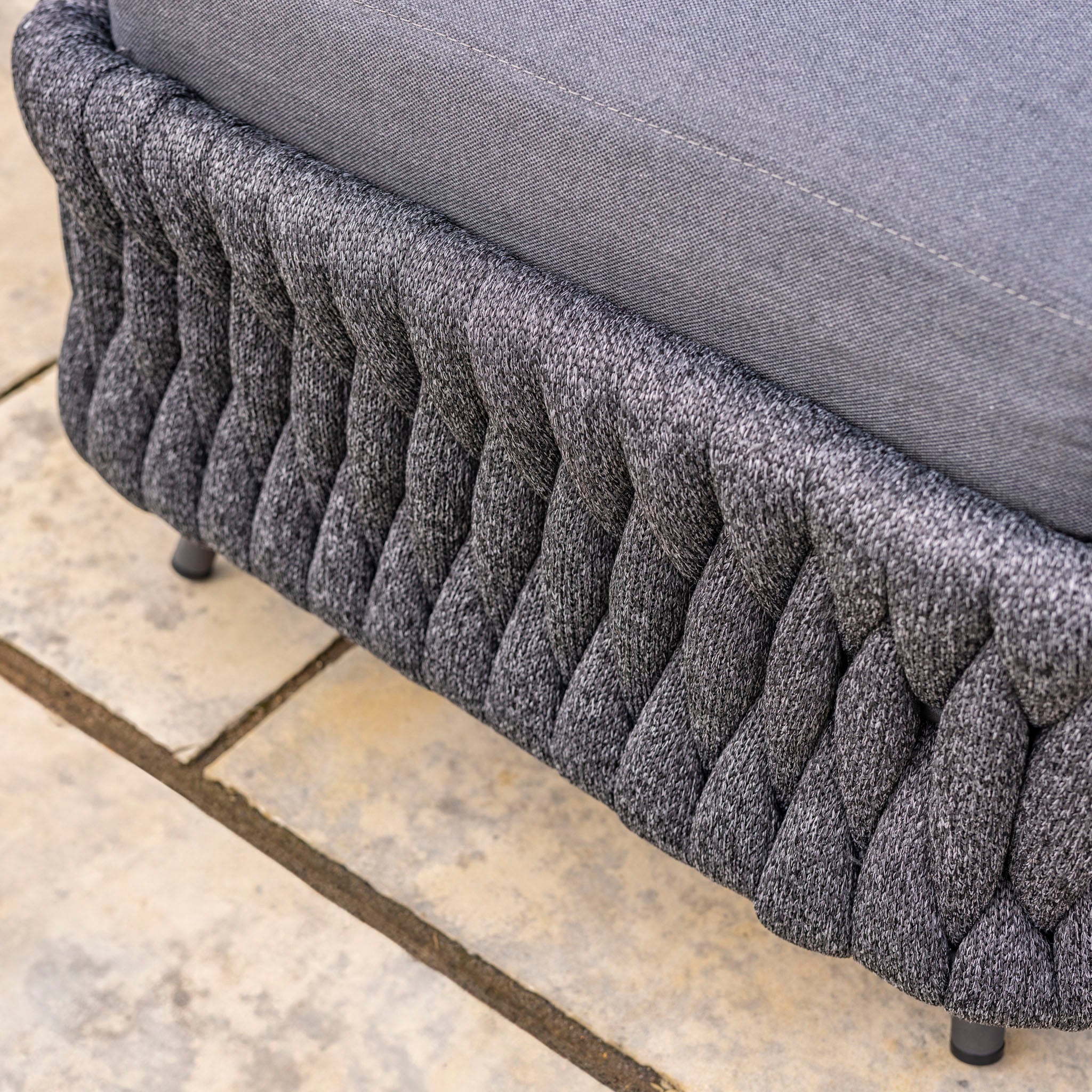 Close-up of a gray, textured fabric sofa base with intricate, wavy patterns, sitting on a light-colored tile floor, reminiscent of the sophisticated design seen in the Palma Rope Rectangular Corner Dining Set with Rising Firepit Table in Grey (Right Hand).