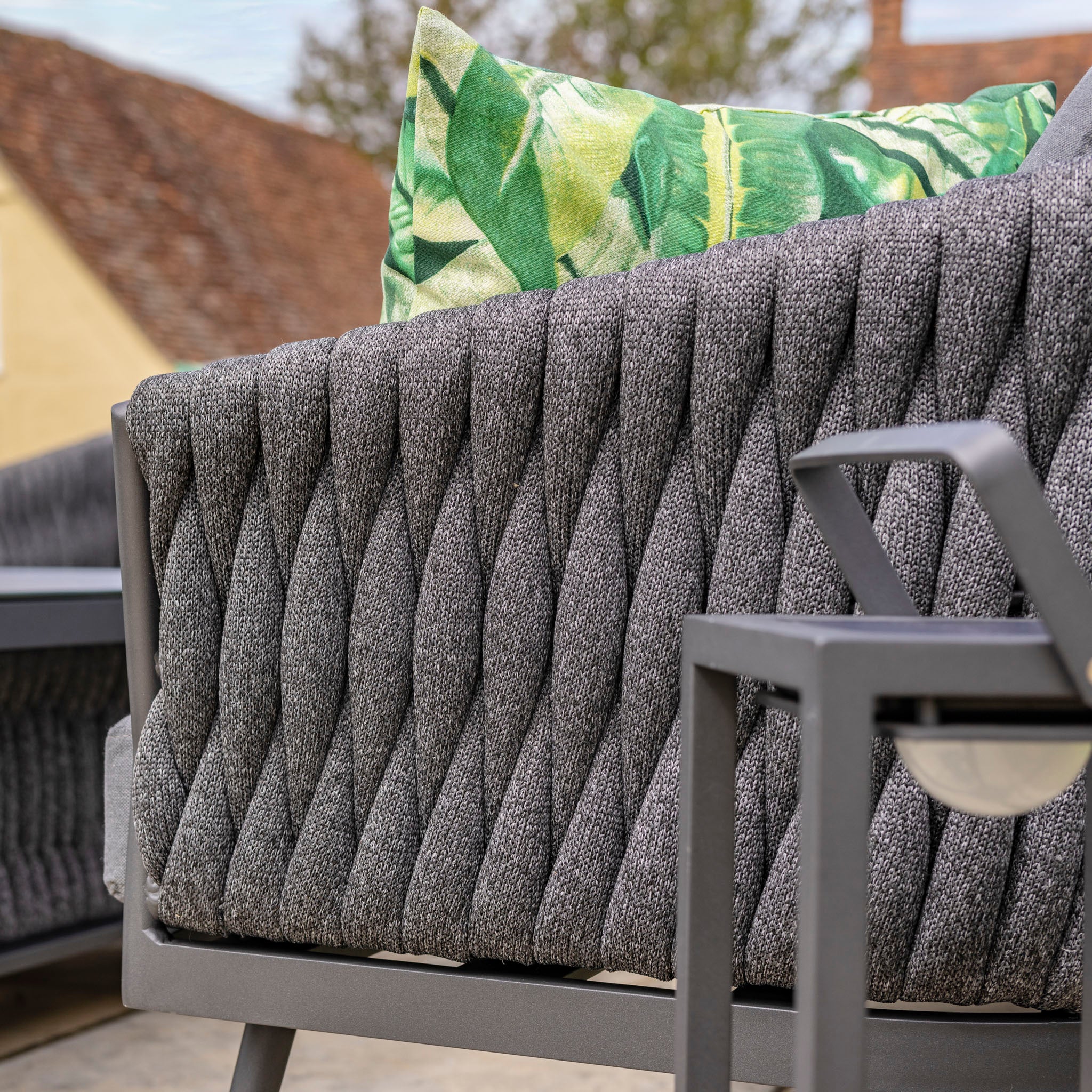 Close-up of a gray outdoor lounge chair with a green leaf-patterned cushion on the backrest, featuring an elegant design that complements the Palma Rope Rectangular Corner Dining Set with Rising Firepit Table in Grey (Right Hand)'s water-repelling thick rope weave and sturdy aluminum frames.