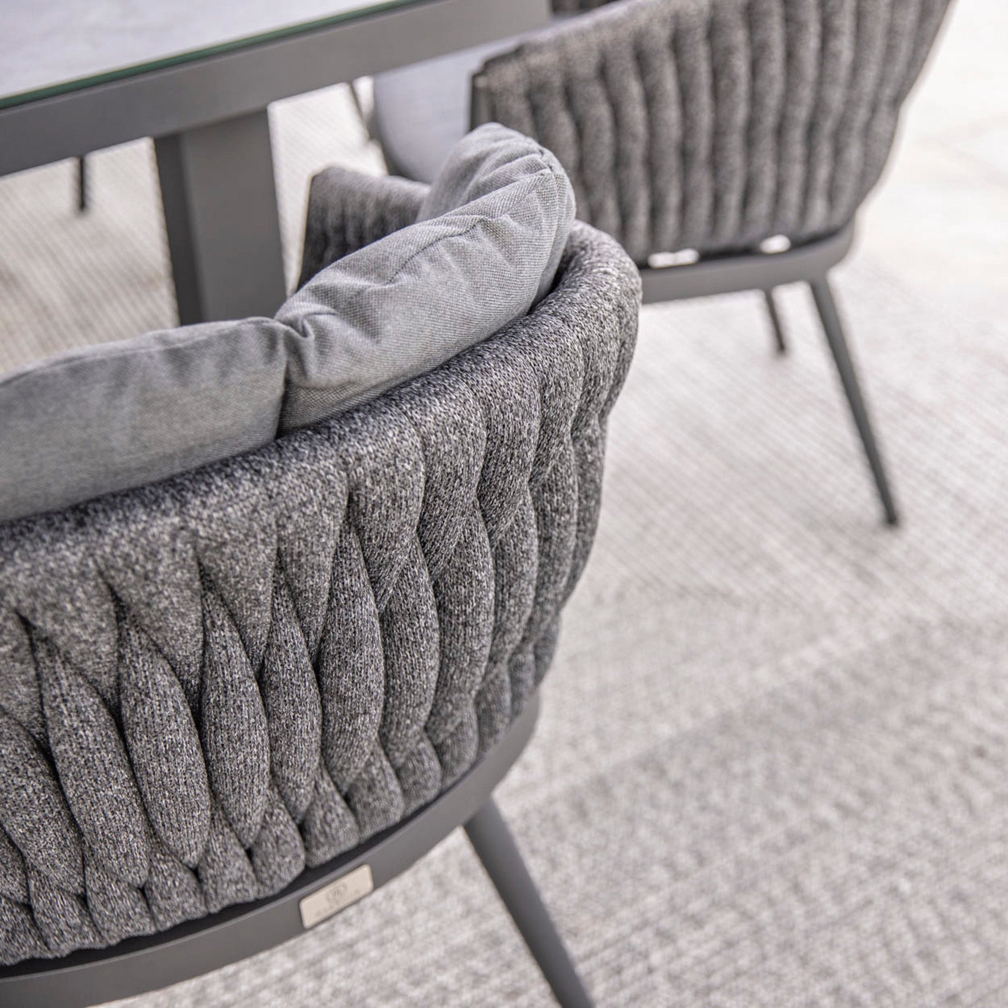 Close-up of two UV resistant modern gray fabric chairs with textured upholstery around the Palma 8 Seat Rope Rectangular Ceramic Firepit Dining Set in Grey, placed on a textured rug.
