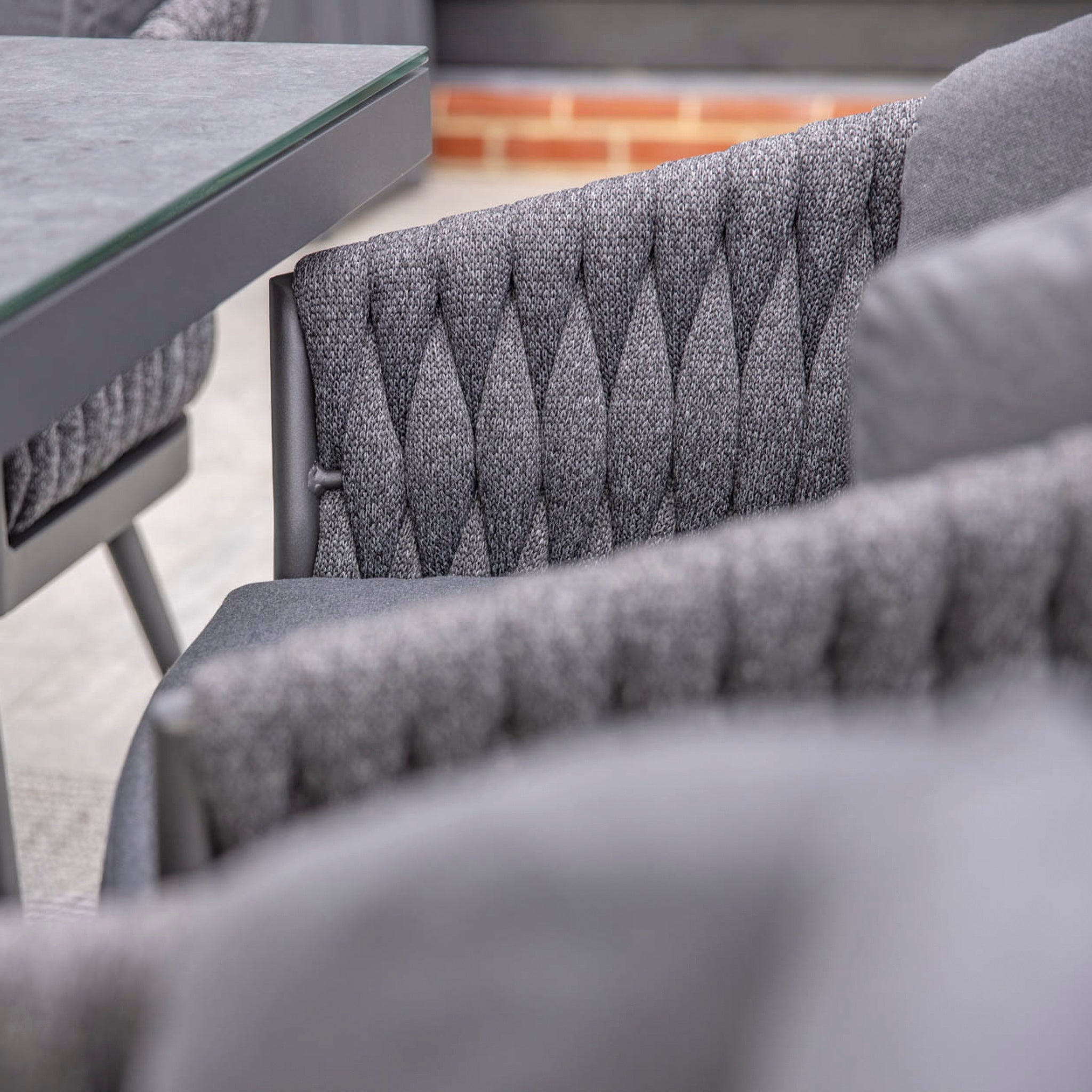 Close-up of grey, UV resistant chairs with diamond-pattern upholstery next to a table in an outdoor setting, part of the Palma 8 Seat Rope Rectangular Ceramic Firepit Dining Set in Grey.