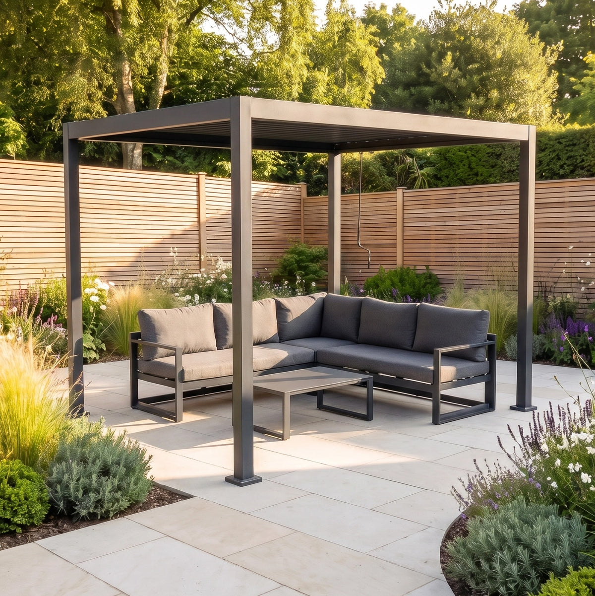 PergoSTET Lite 2.4m x 3m Metal Rectangular Pergola in Grey with gray sofa and table on a plant-filled patio.