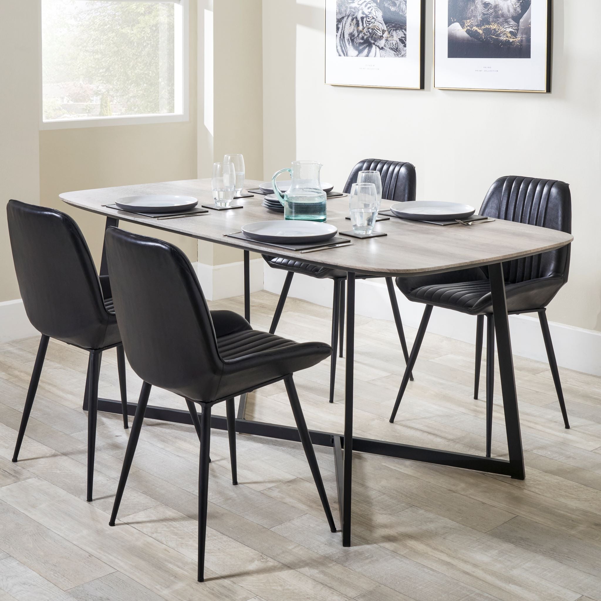 Bright room adorned with framed art featuring a modern dining table set, complemented by four Angelo Leather and Iron Retro Dining Chairs in Steel Grey from Pacific Lifestyle, complete with plates and a glass pitcher.