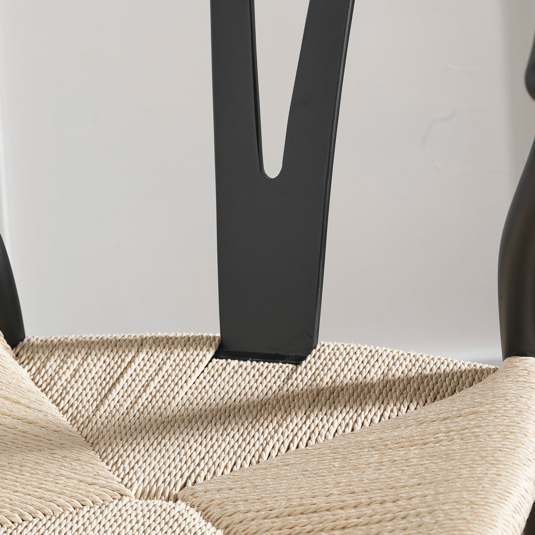 A close-up of the Pacific Lifestyle - Quinn Black Beech Wood and Natural Rope Dining Chair seat crafted from woven natural rope, complemented by a sleek black metal backrest in a minimalist setting.