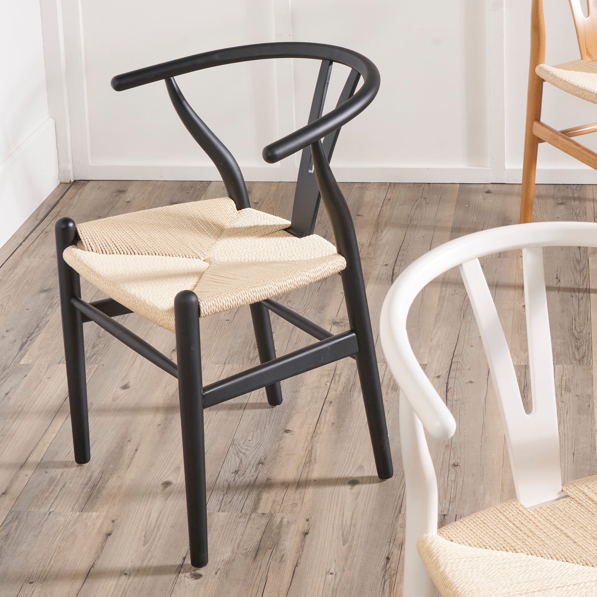 The Pacific Lifestyle - Quinn Dining Chair, made of black beech wood with a natural rope seat, rests elegantly on a wooden floor amidst matching chairs.
