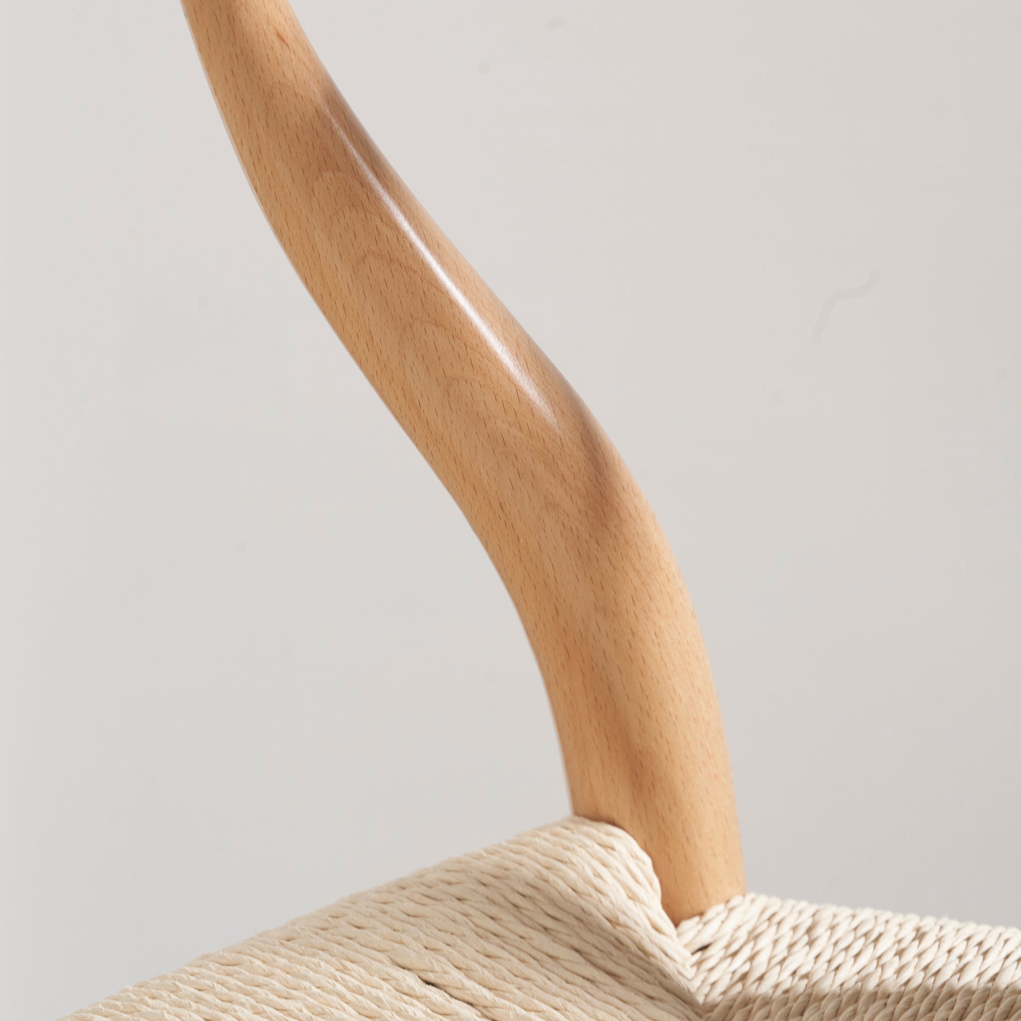 Close-up of a curved wooden handle on a woven basket, echoing the natural beech wood and rope of a Pacific Lifestyle - Quinn Dining Chair, against a plain white background.