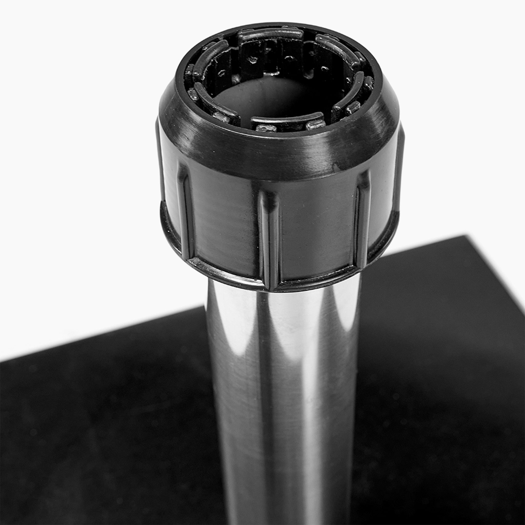 Close-up of the Pacific Lifestyle Rome Polished Black Granite 60KG Wheeled Parasol Base, showcasing its metal cylindrical form with a black ridged cap, reminiscent of sleek stainless steel tubes, resting on a black surface.