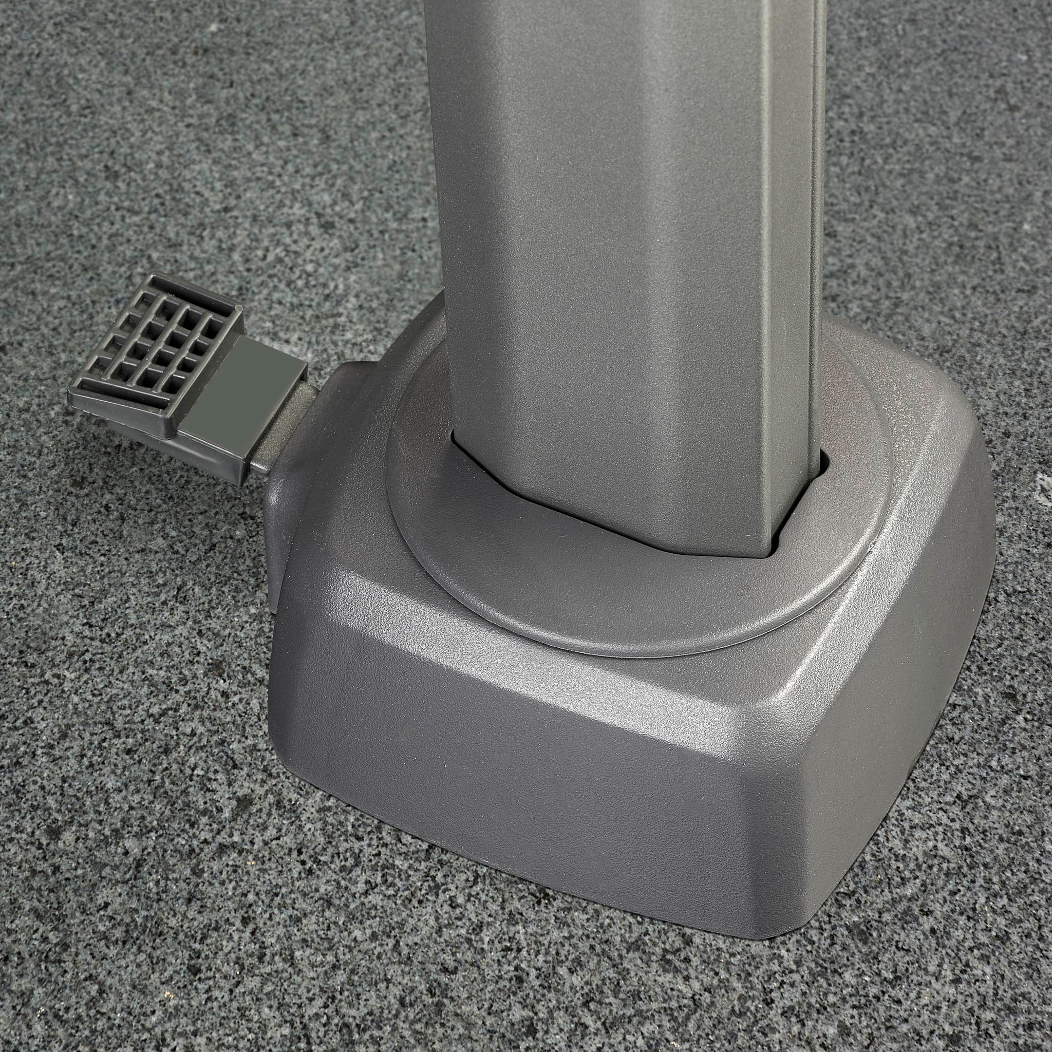 Close-up of a gray metal base with a pedal on a textured floor, designed to support the Challenger T2 3.5m x 2.6m Rectangular Cantilever Parasol in Champagne, featuring 360-degree rotation for versatile outdoor shade.