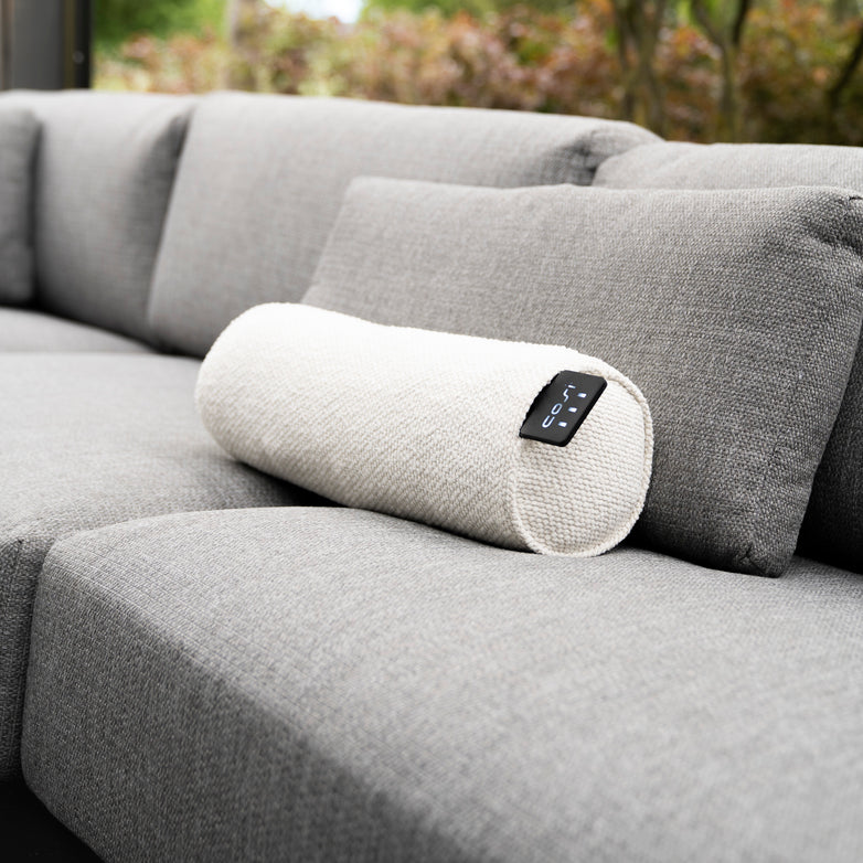 The Cosi - Cosipillow Heated Bolster in Teddy is a gray sofa accessory with a light beige cylindrical design, featuring an infrared heating element and small control panel, providing ultimate relaxation.