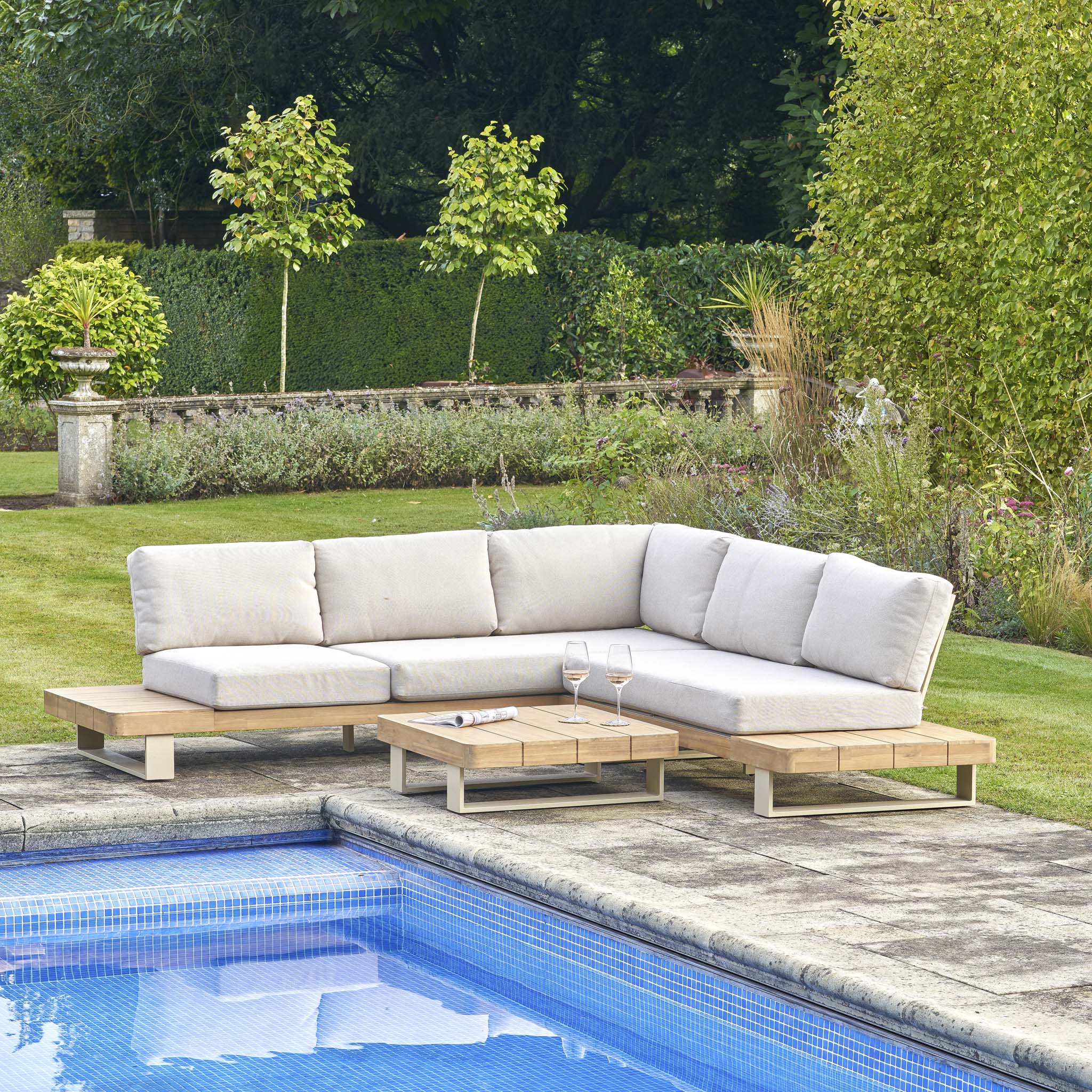 Pacific Lifestyle - Osaka Corner Sofa Set in Latte, crafted from sustainable acacia wood, is placed by a pool with a coffee table, wine glasses, and surrounded by lush greenery.