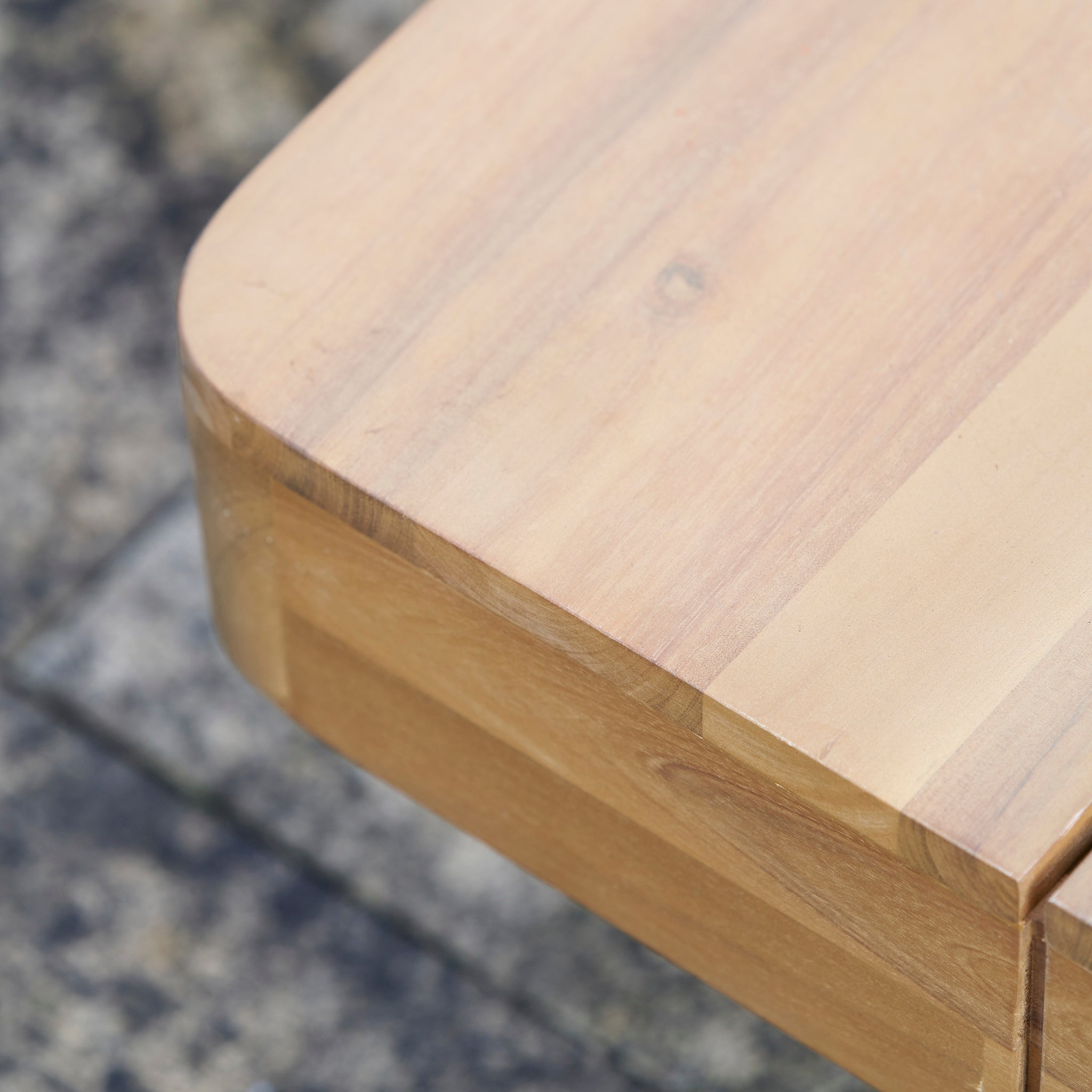 Close-up of a light brown acacia wood surface with a rounded edge—crafted sustainably to beautifully complement the Pacific Lifestyle - Osaka Corner Sofa Set in Latte and other outdoor furniture.
