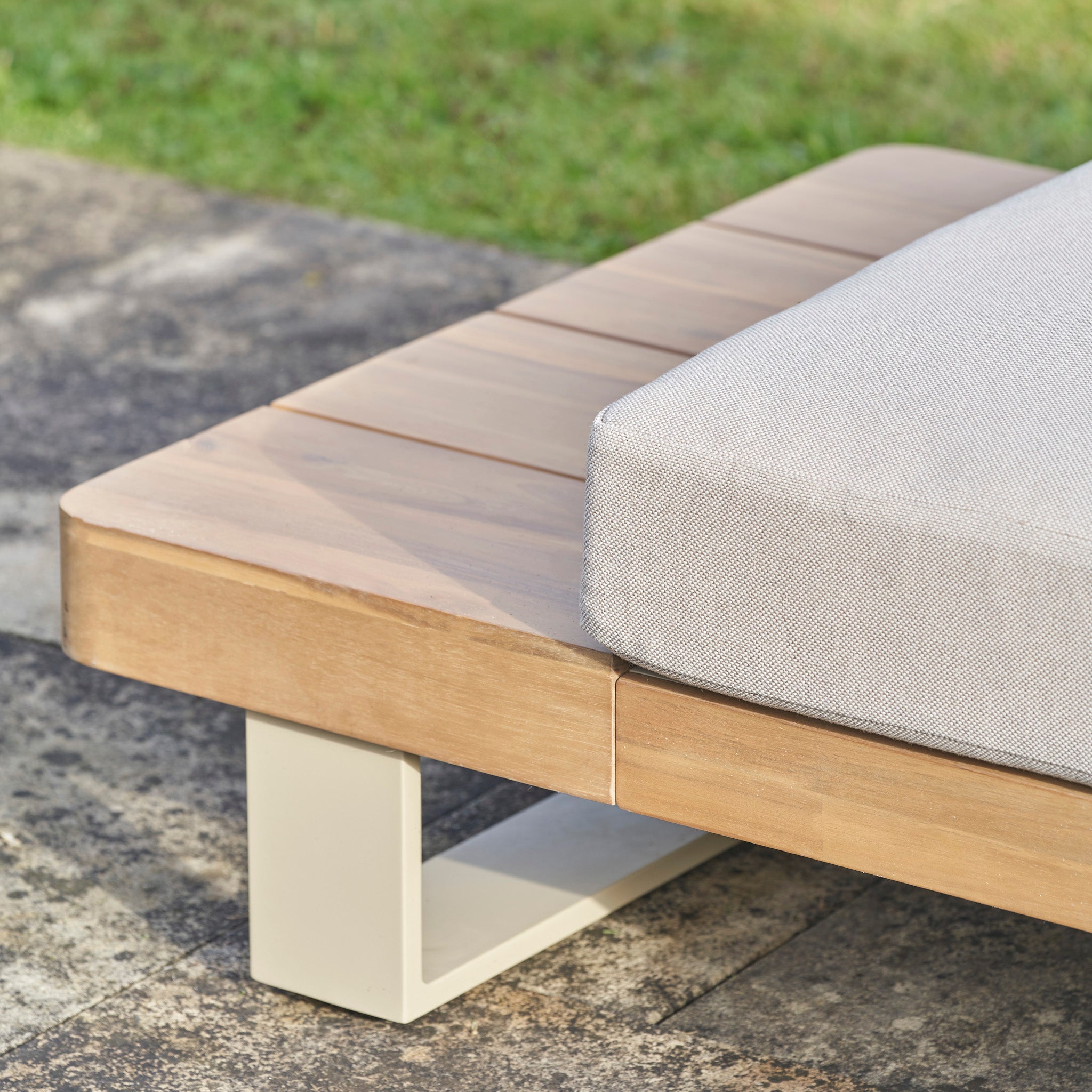 Close-up of the Pacific Lifestyle Osaka Corner Sofa Set in Latte, crafted from sustainable acacia wood with a light gray cushion, placed on a stone patio near grass.