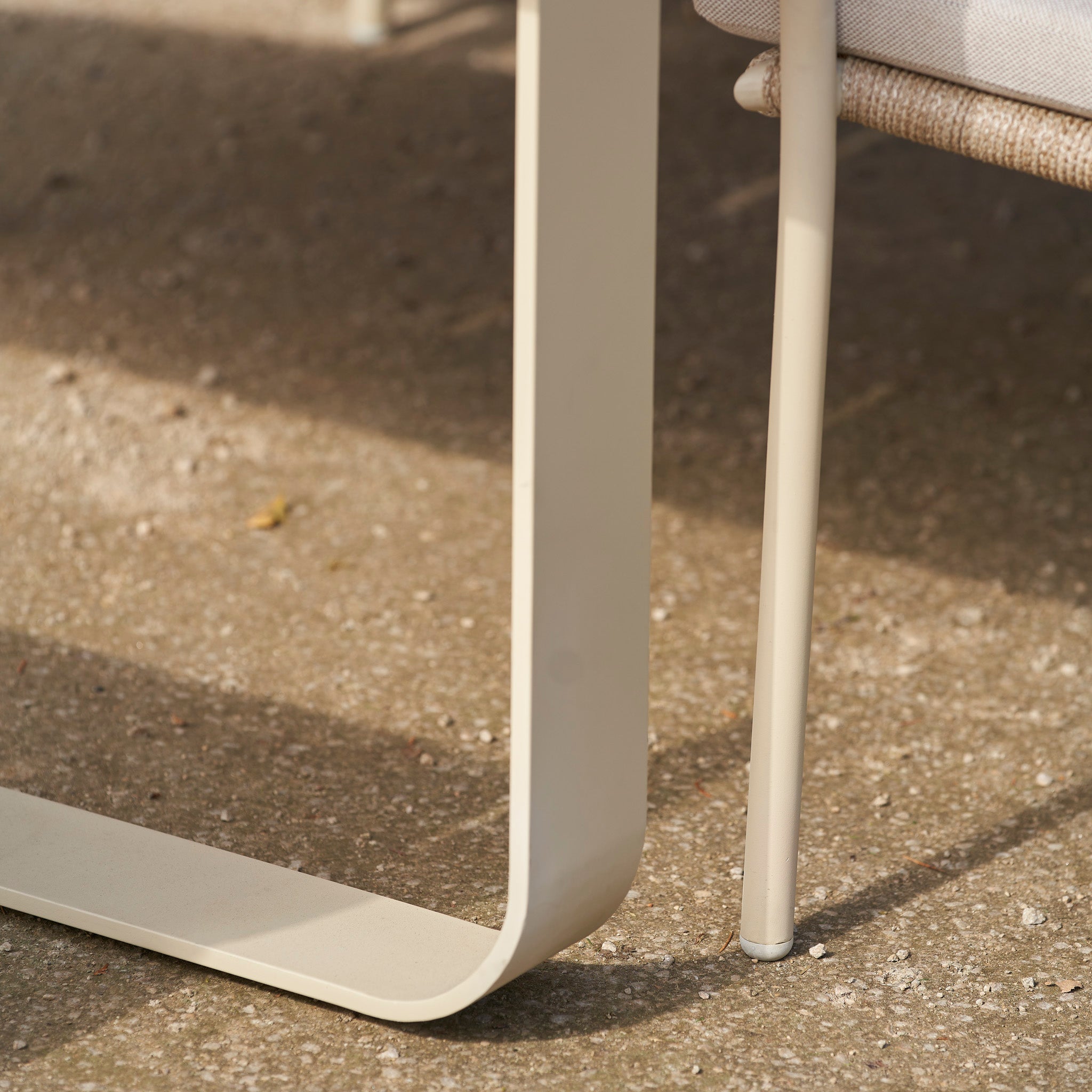 Close-up of the metal legs and frame of a beige chair from the Pacific Lifestyle - Osaka 6 Seat Dining Set in Latte, placed on a textured concrete surface.