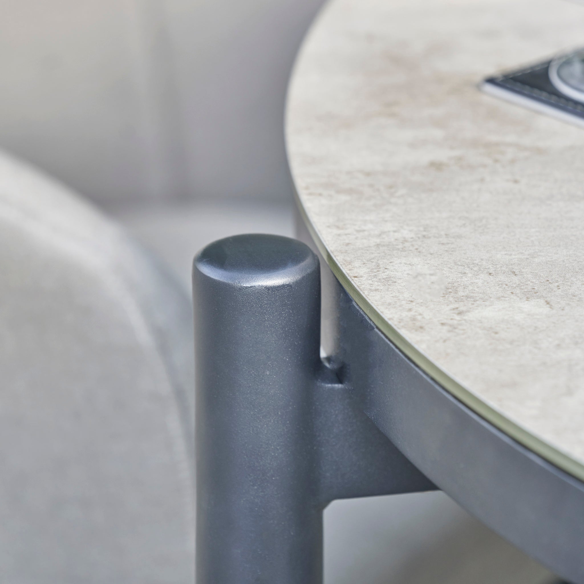 Close-up of a round table corner from the Kai 4 Seat Round Dining Set in Light Grey, showcasing a sturdy metal leg and a smooth, light-colored tabletop—ideal for creating an elegant outdoor dining space.