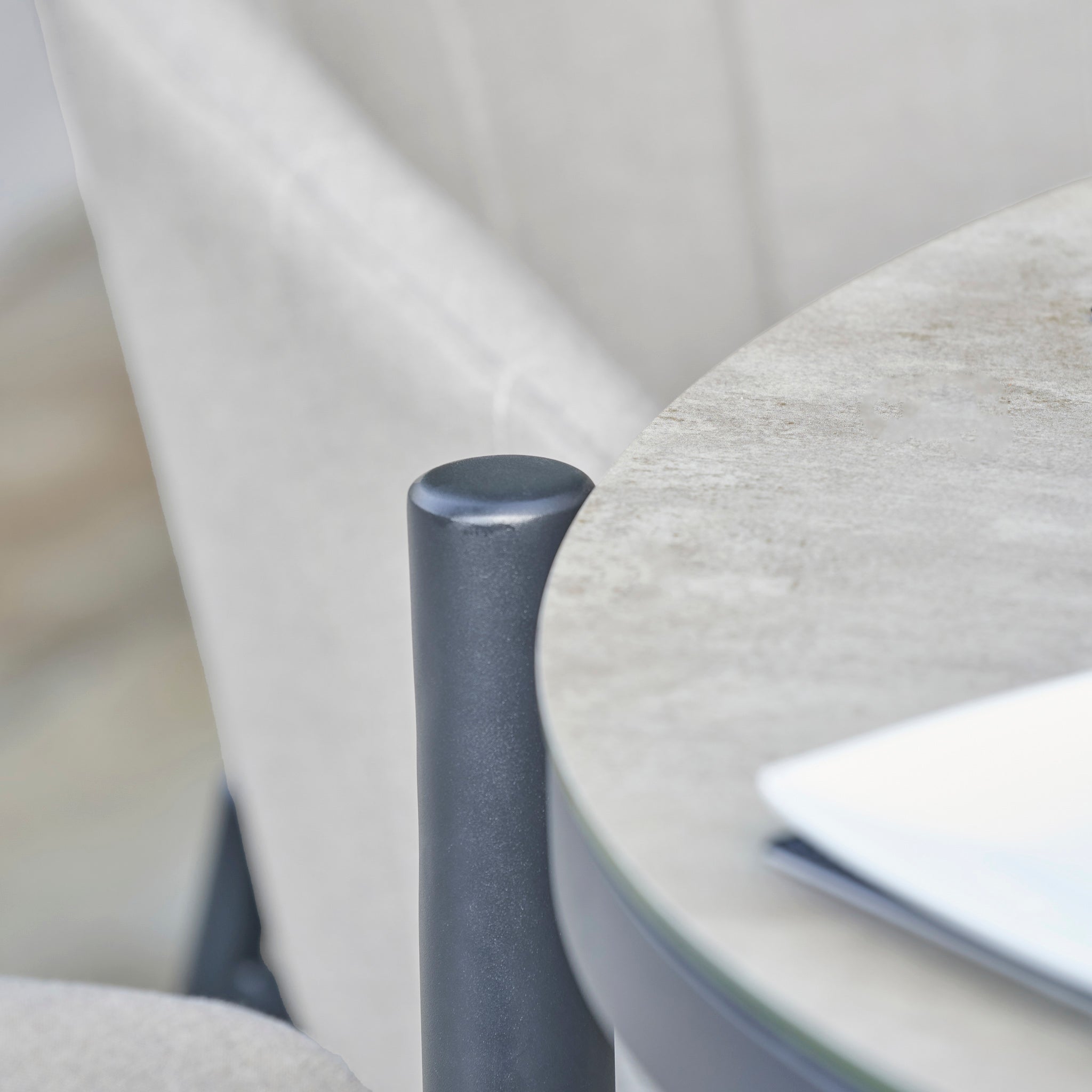 Close-up of the Kai 4 Seat Round Dining Set in Light Grey, featuring a chair and some papers, all in neutral tones—perfect for those looking for stylish light grey garden furniture to enhance any outdoor space.