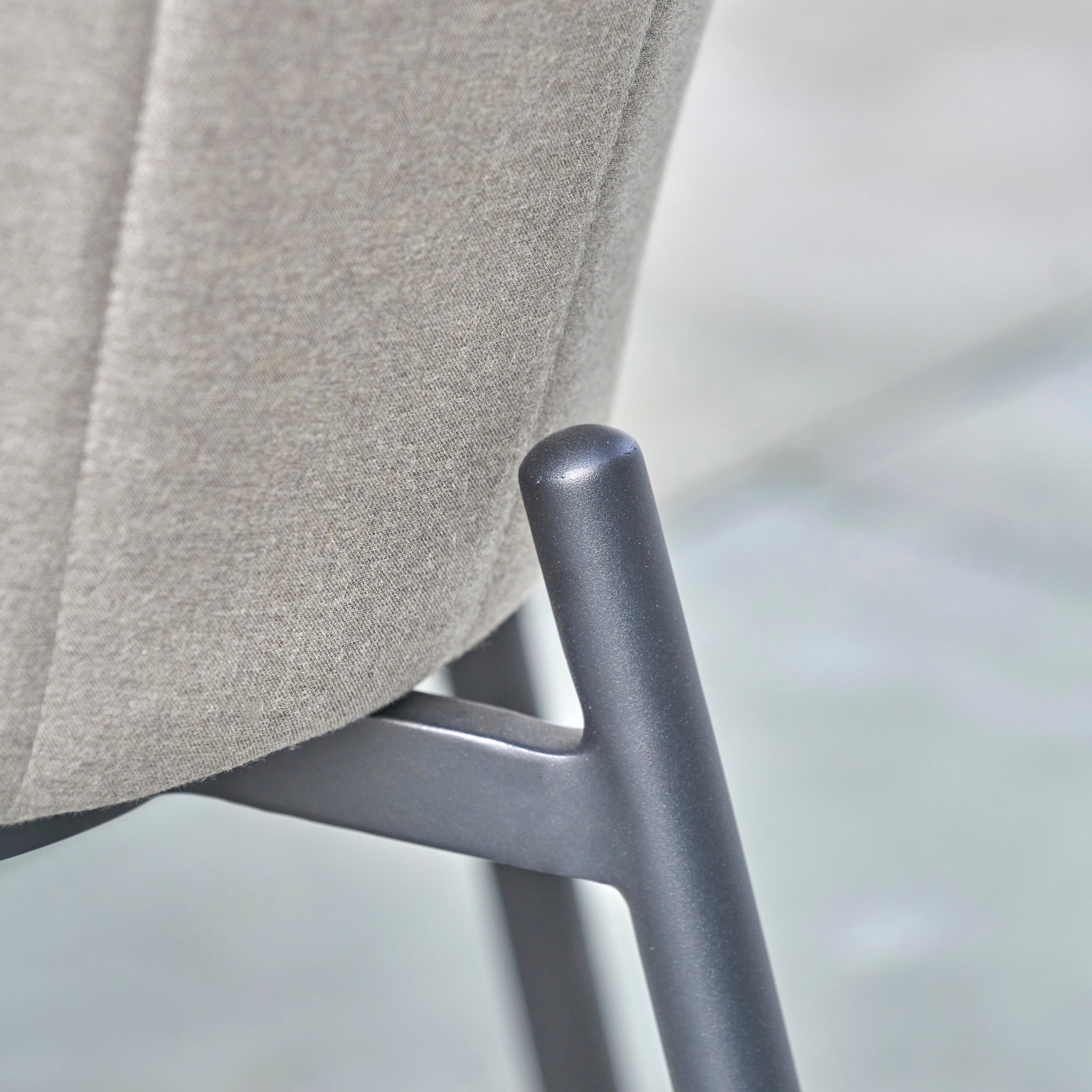 Close-up of a gray metal chair leg and the edge of a cushioned beige fabric seat, part of the Kai 4 Seat Round Dining Set in Light Grey—an elegant choice for outdoor dining.
