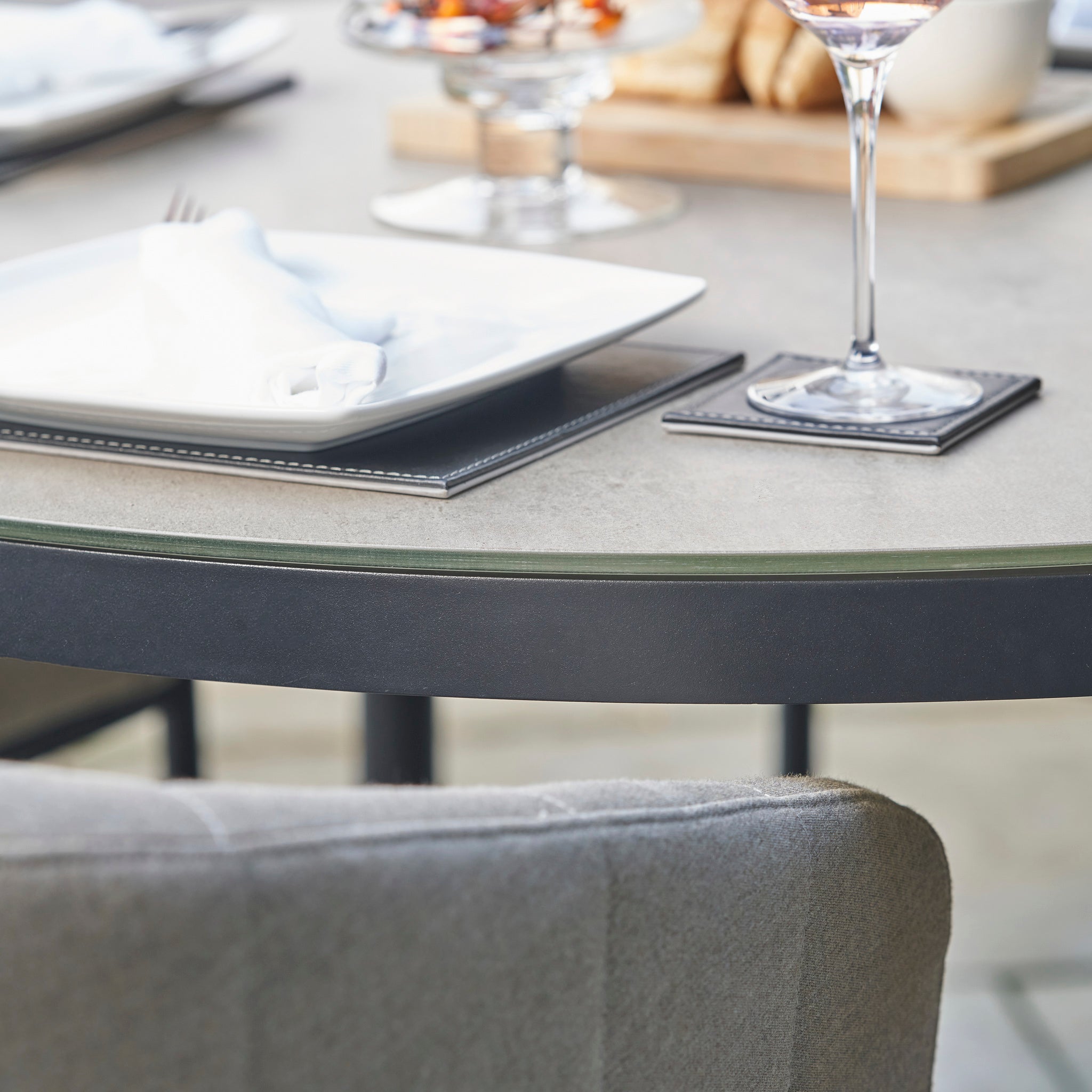 Close-up of a table set with a plate, napkin, glass of rosé wine, and blurred food in the background—an inviting scene perfect for the Kai 4 Seat Round Dining Set in Light Grey, effortlessly combining style and comfort for any small patio gathering.