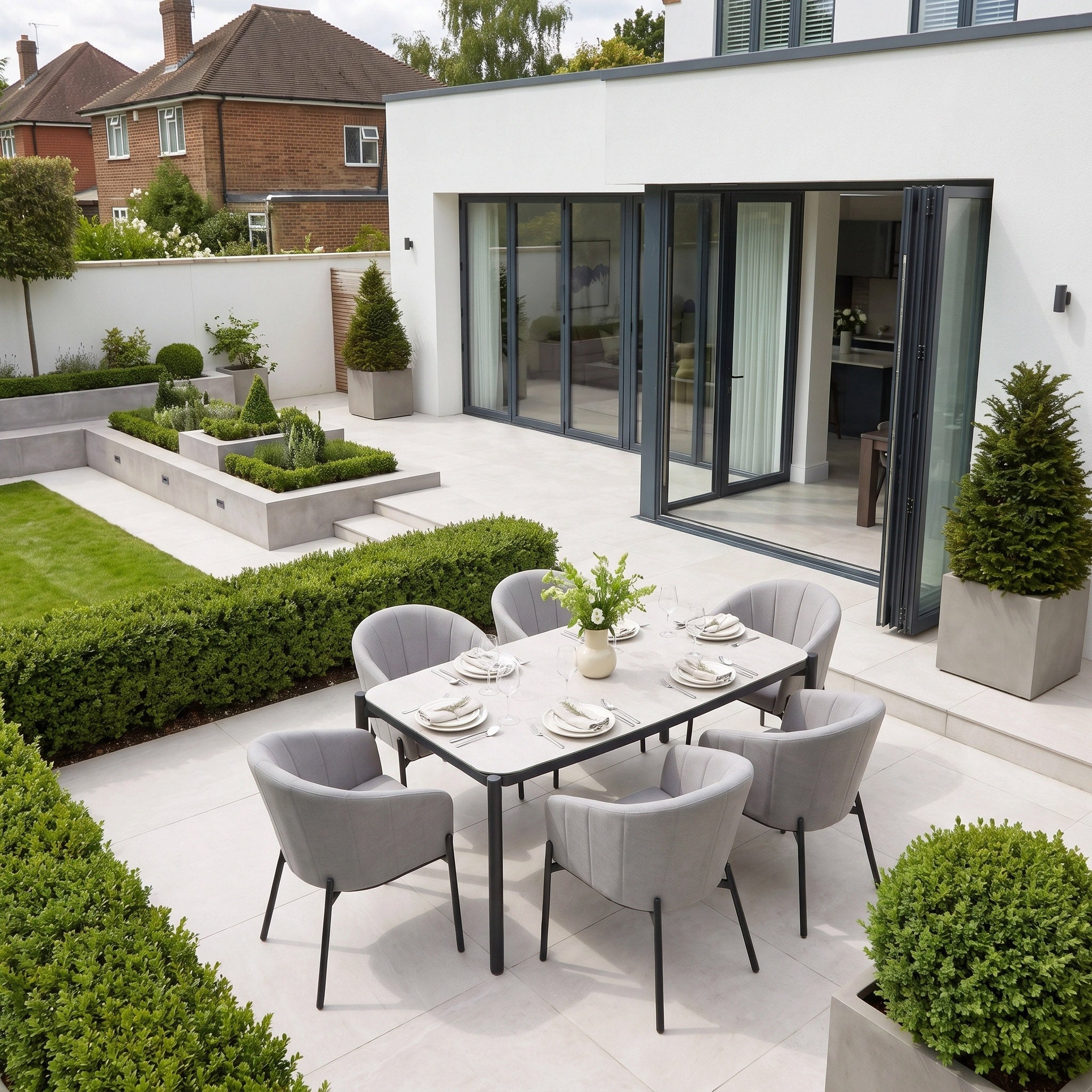Create a modern patio with the Kai 6 Seat Rectangular Dining Set in Light Grey, featuring a powder-coated aluminium frame, six gray chairs, potted plants, and manicured garden hedges—perfect for stylish outdoor dining.