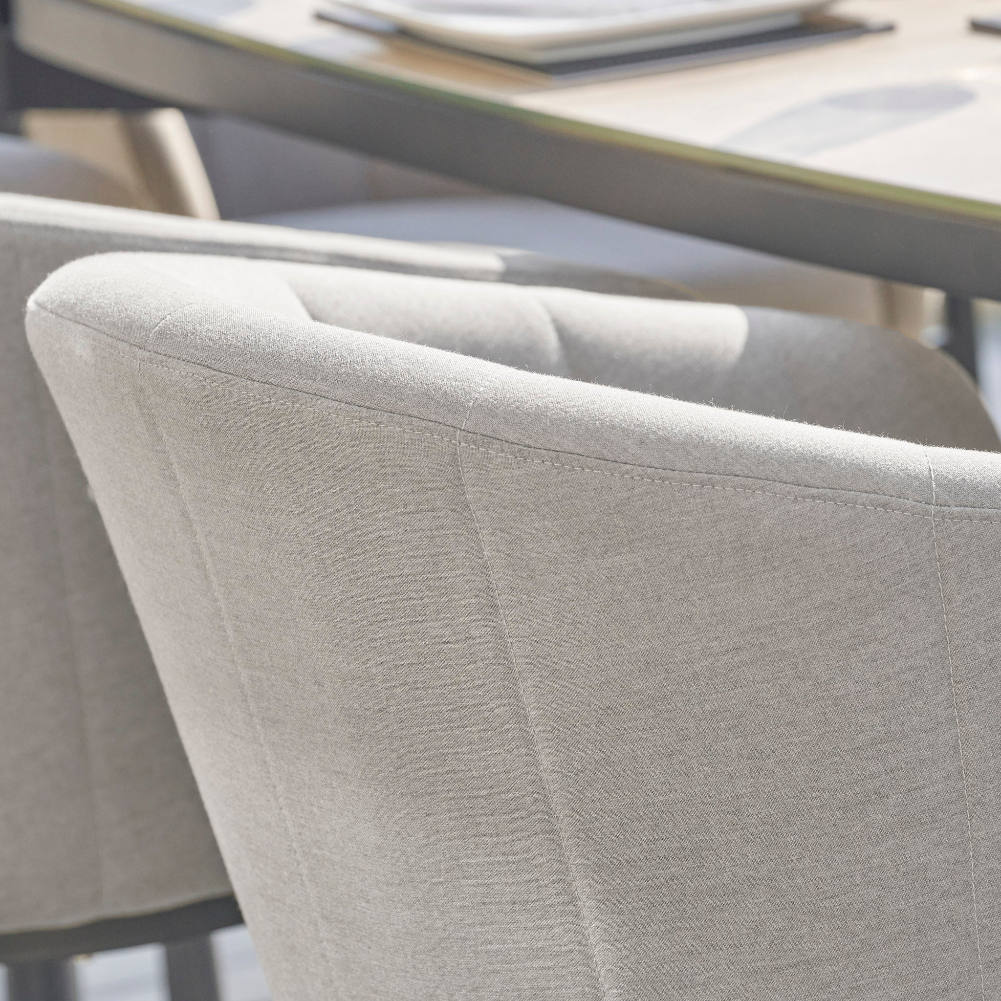 Close-up of the Kai 6 Seat Rectangular Dining Set in Light Grey, with sunlight streaming across its sophisticated upholstery and table surface adorned with documents, evoking the comfort and elegance of premium garden furniture.