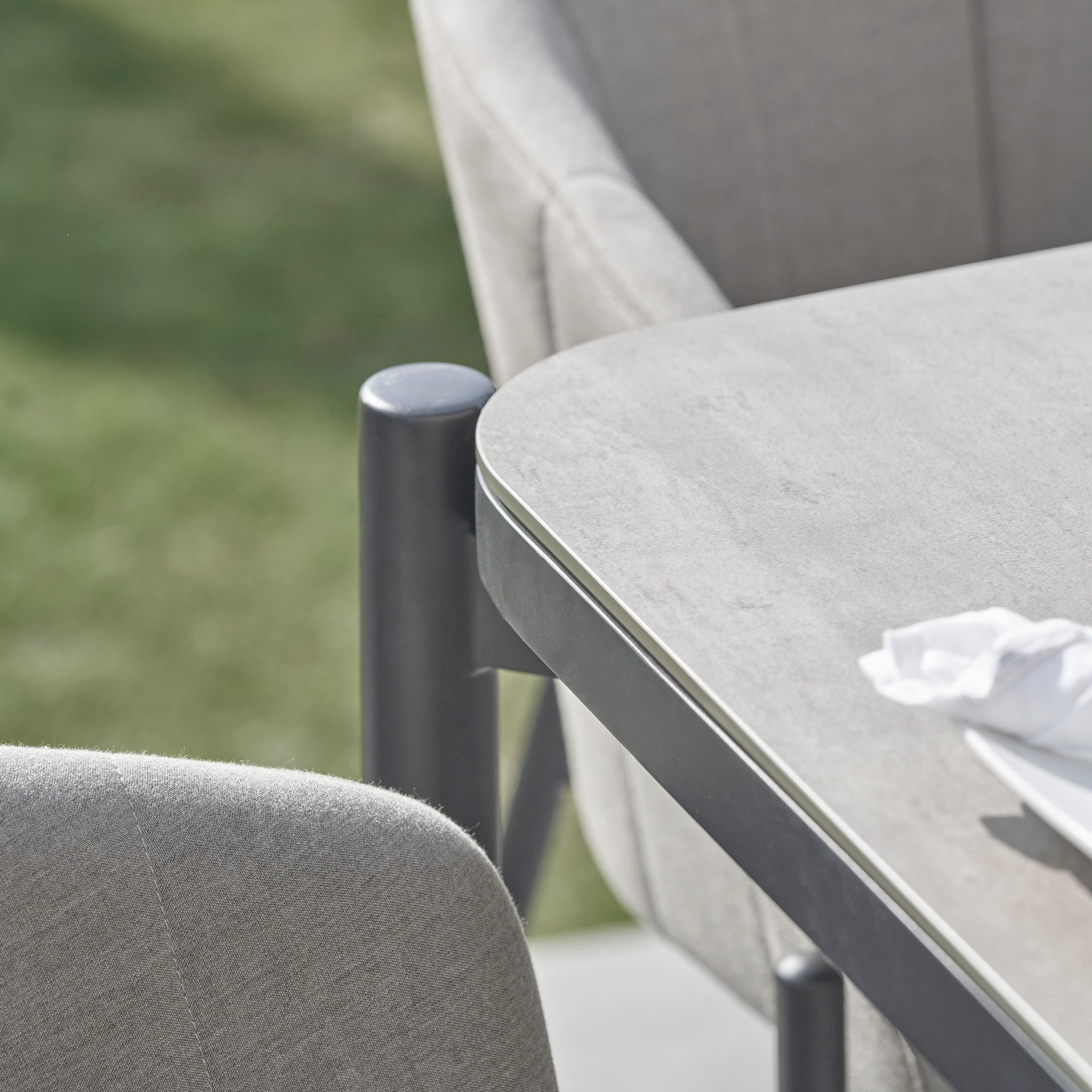 Close-up of the Kai 6 Seat Rectangular Dining Set in Light Grey, featuring a table and chairs with a napkin, against a backdrop of blurred green grass.