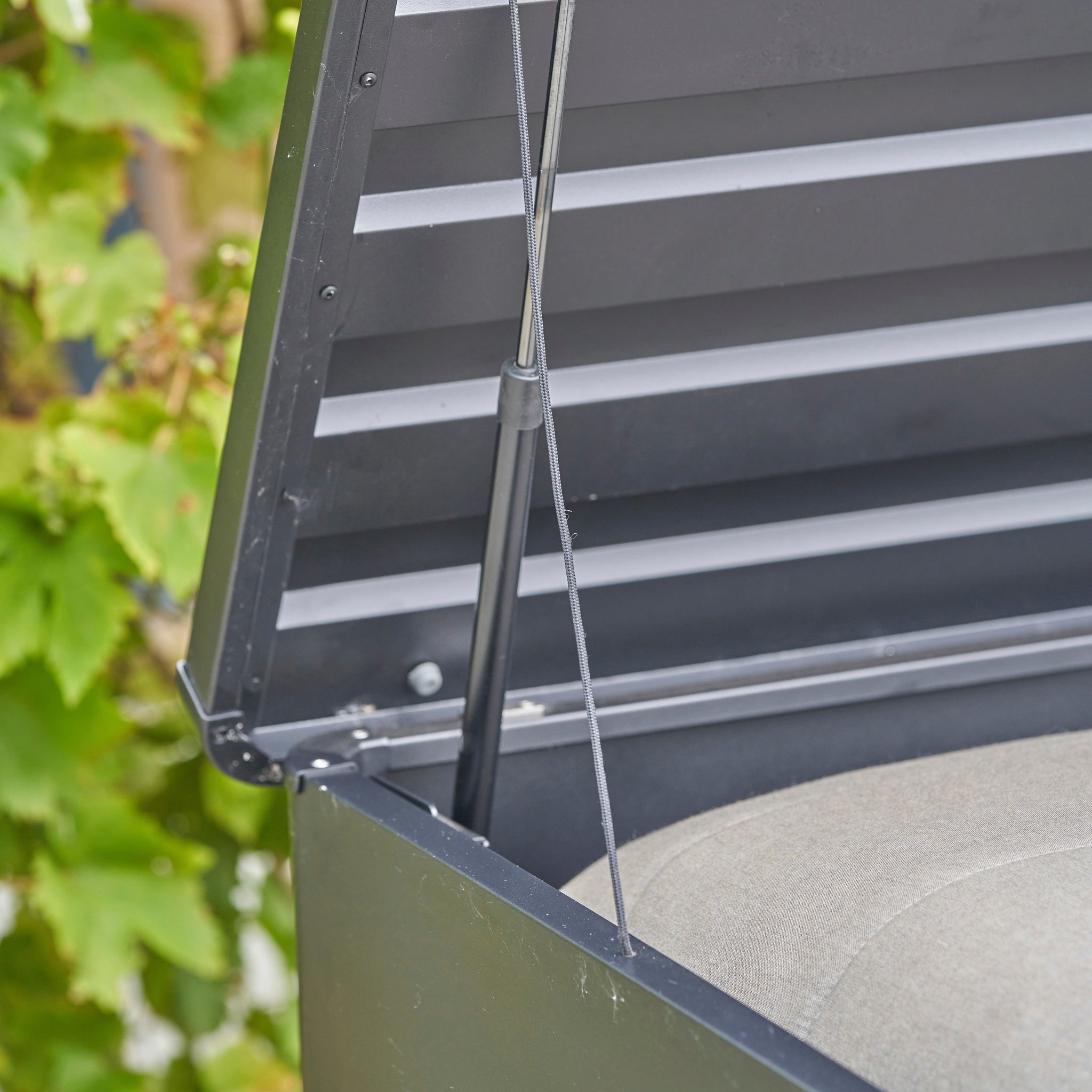 Close-up of the Pacific Lifestyle - Rhode Island Large Outdoor Cushion Box in Anthracite, shown with lid open and supported by a hydraulic strut.