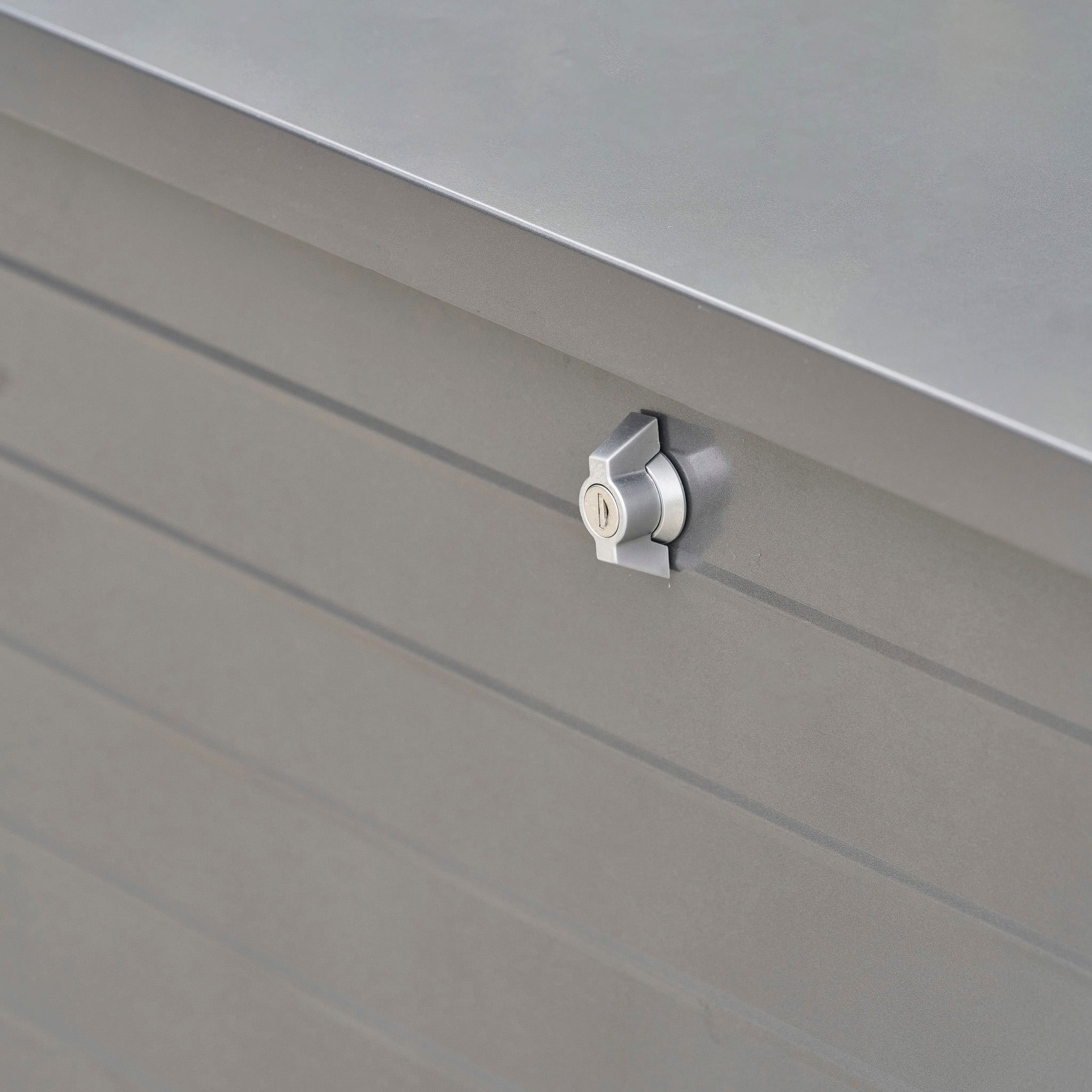 Close-up of a silver metal lock on the gray panel surface of the Pacific Lifestyle - Rhode Island Small Outdoor Cushion Box in Anthracite.