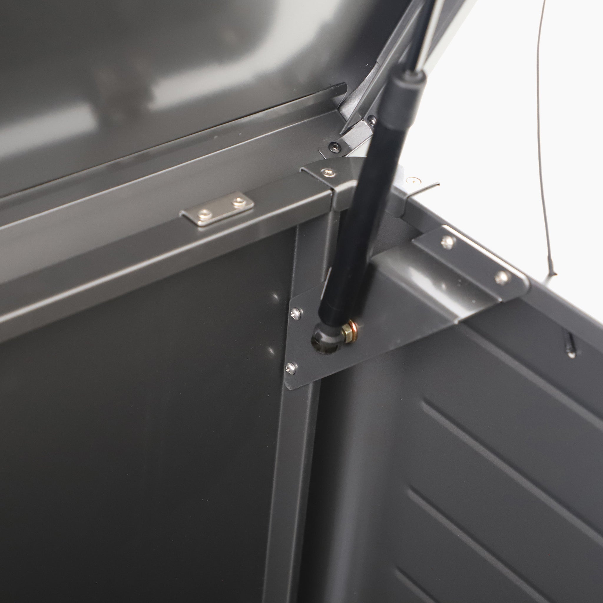Close-up of a metal hinge and hydraulic support arm inside the Pacific Lifestyle - Rhode Island Large Outdoor Cushion Box in Black, crafted from galvanised steel, shown with its lid open.