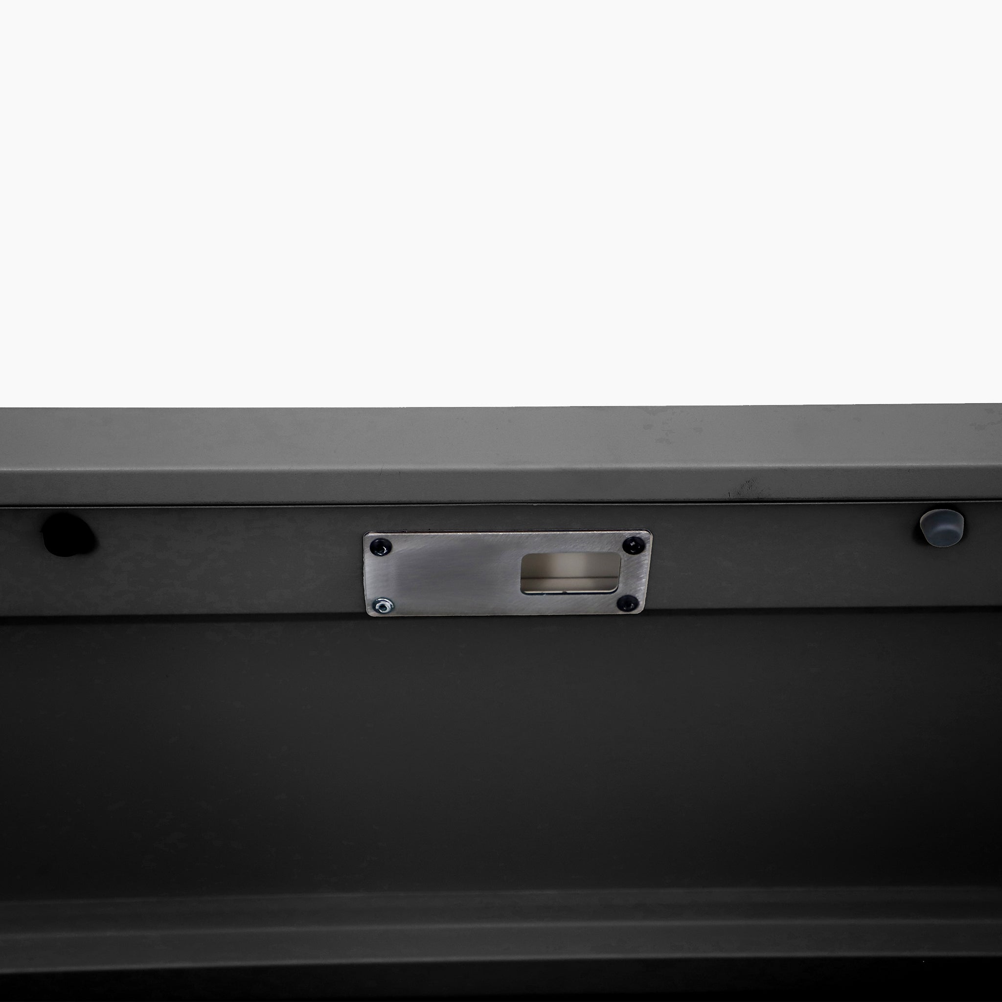 Close-up of the Pacific Lifestyle - Rhode Island Small Outdoor Cushion Box in Black, showing its latch plate and screws on a dark gray surface, set against a plain white background.