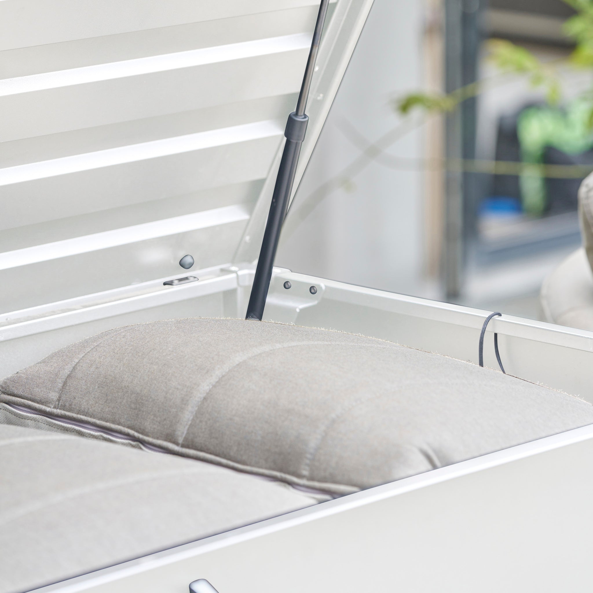 Close-up of the Pacific Lifestyle - Rhode Island Large Outdoor Cushion Box in Pebble, shown with its lid open and a beige cushion inside, supported by a galvanized steel hinge for easy access.