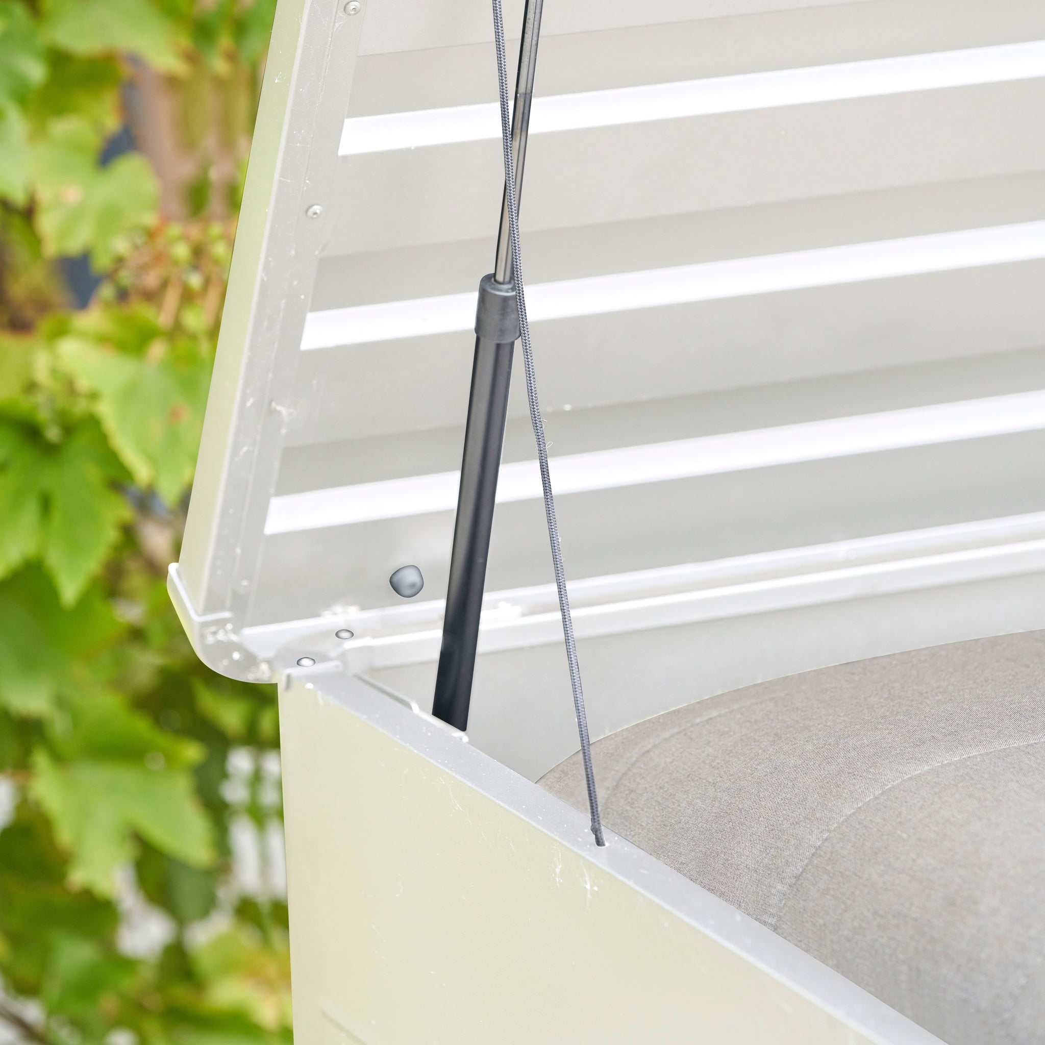 Close-up of a gas lift hinge holding open the Pacific Lifestyle - Rhode Island Large Outdoor Cushion Box in Pebble, made from durable galvanised steel, with a cushion stored inside.