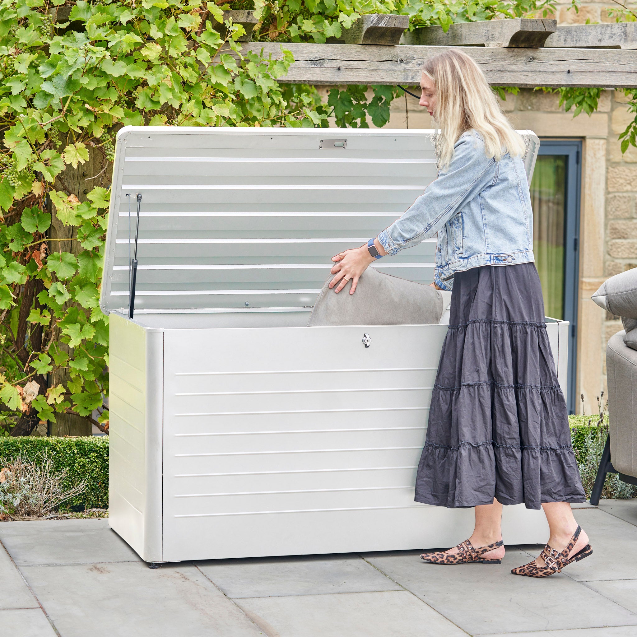 A woman places a cushion inside the Pacific Lifestyle Rhode Island Small Outdoor Cushion Box in Pebble on her patio.