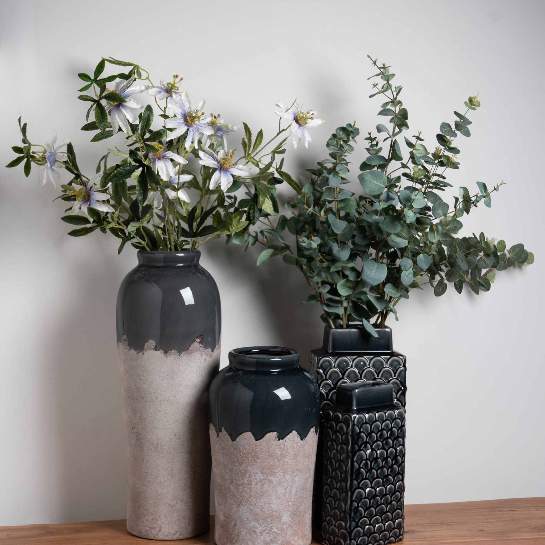 Three vases with different shapes and designs, including a Large Conran Vase featuring a dual textured finish, filled with white and green flowers, displayed on a wooden surface.