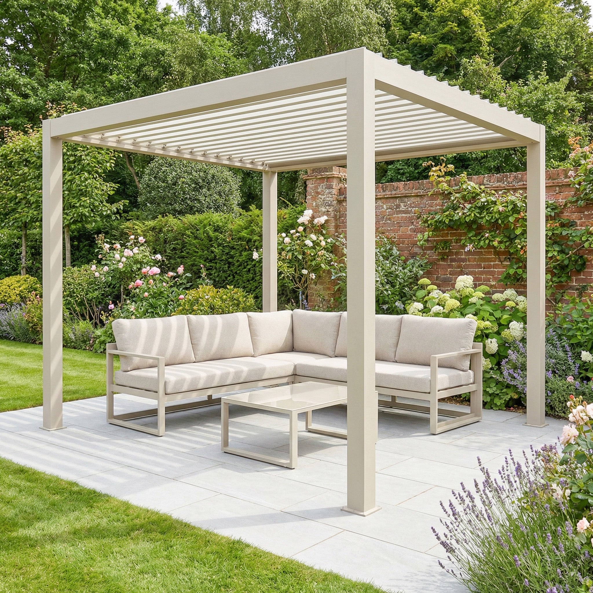 The PergoSTET Lite 2.4m x 3m Metal Rectangular Pergola in Latte sits on a patio with a beige outdoor sofa and glass table, surrounded by greenery and flowers.