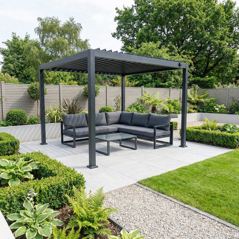 The PergoSTET Lite 2.4m x 3m Metal Rectangular Pergola in Grey shelters a gray outdoor sofa and table on a tiled patio, surrounded by lush green garden plants.