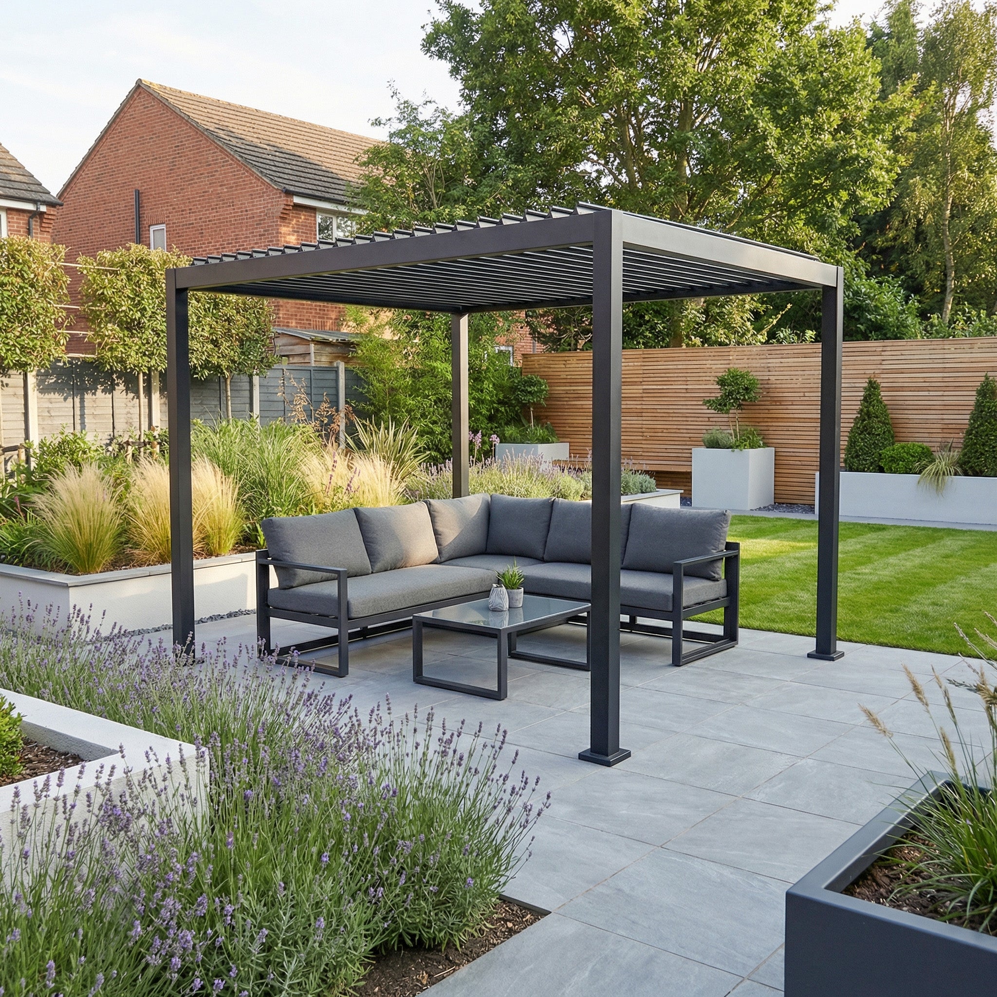 The PergoSTET Lite 2.4m x 3m Metal Rectangular Pergola in Grey features tilting louvres for outdoor shade over a gray patio sofa, set amid lush plants and green lawn.