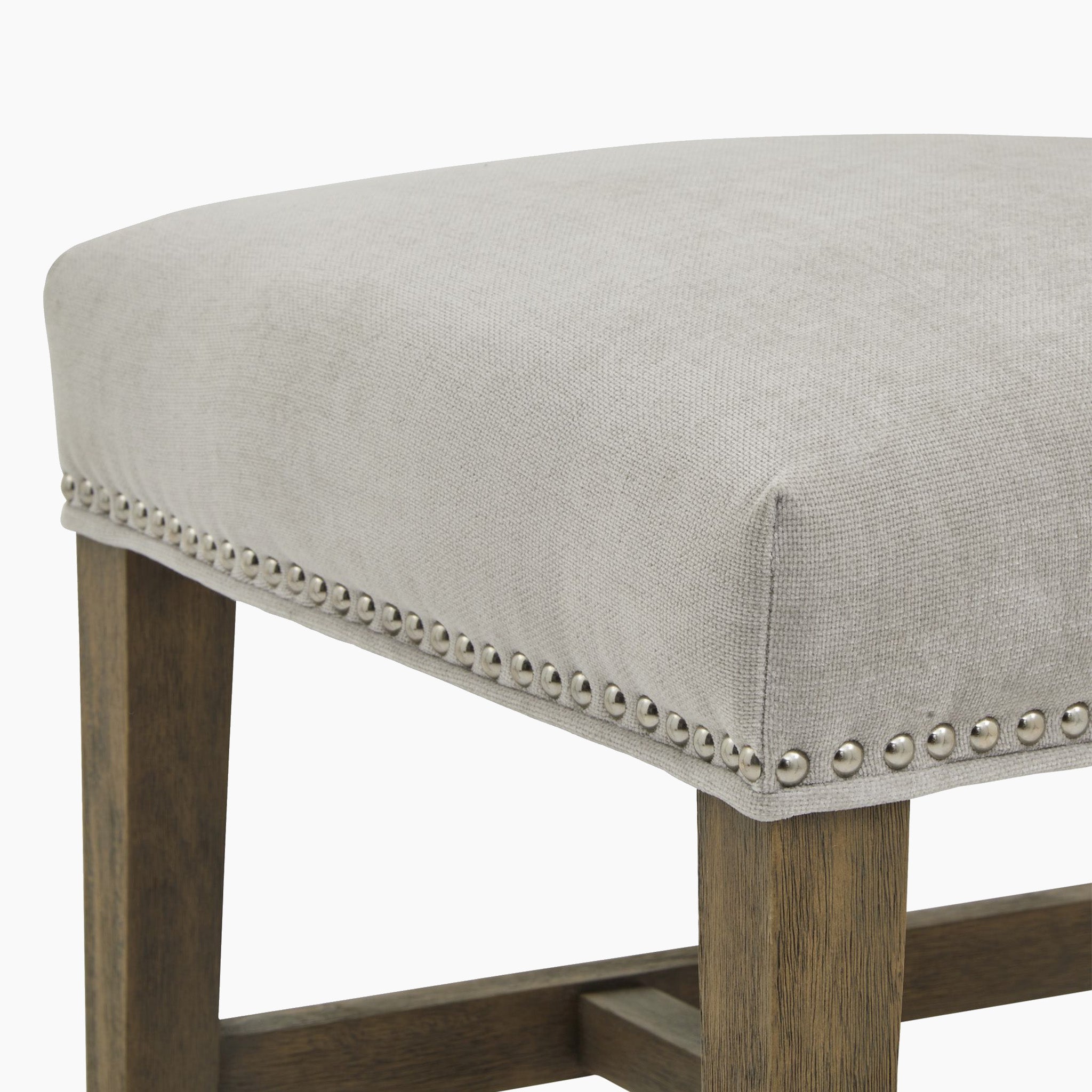 A close-up view of the Cobham Grey Dining Chair, showcasing its luxurious grey upholstery, complemented by a wooden base and detailed with nailhead trim.