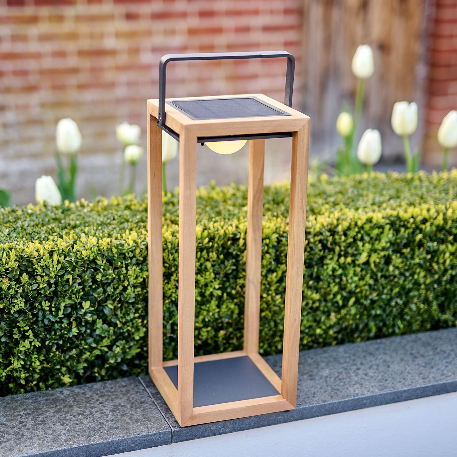 Luxor Floor Outdoor and Indoor Solar Lantern in Teak, standing on a patio, providing warm ambient light after dark.